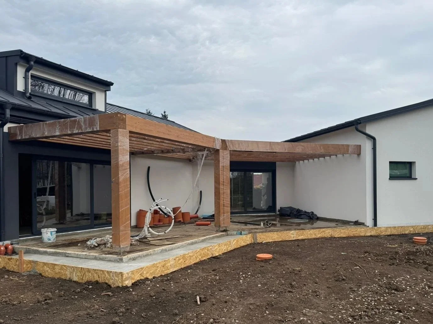Construction site of a modern house with ongoing work on the patio and roof structure, tools and building materials scattered around.