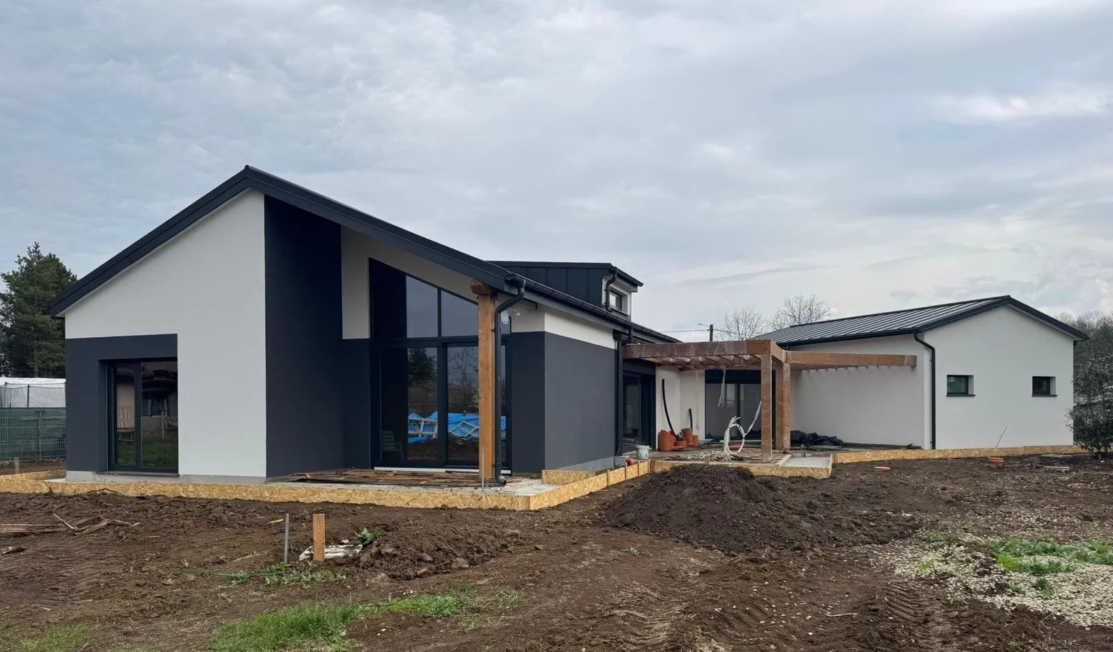Modern house under construction with black and white exterior, large windows, and a wooden deck area in the backyard.