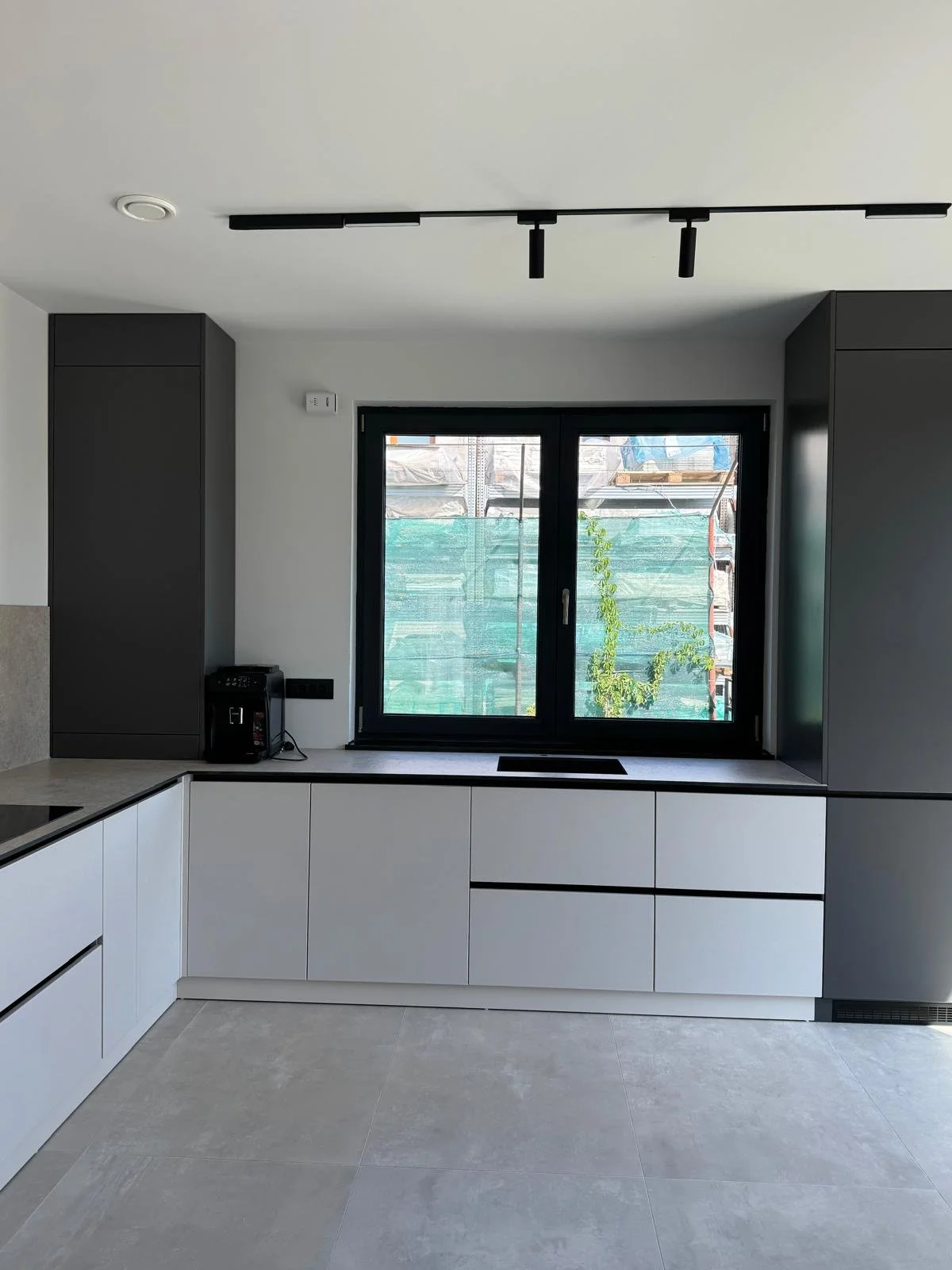 Modern kitchen with white lower cabinets, dark gray upper cabinets, and a large window with a view outside.