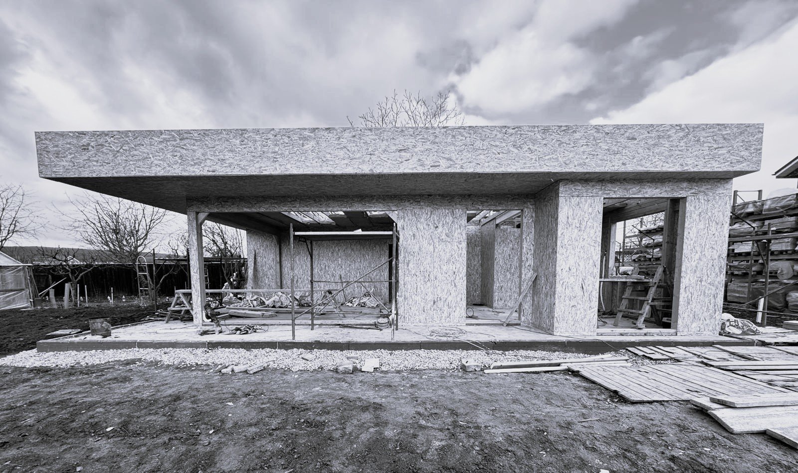 Under construction house with wooden framing and scaffolding, cloudy sky in background.