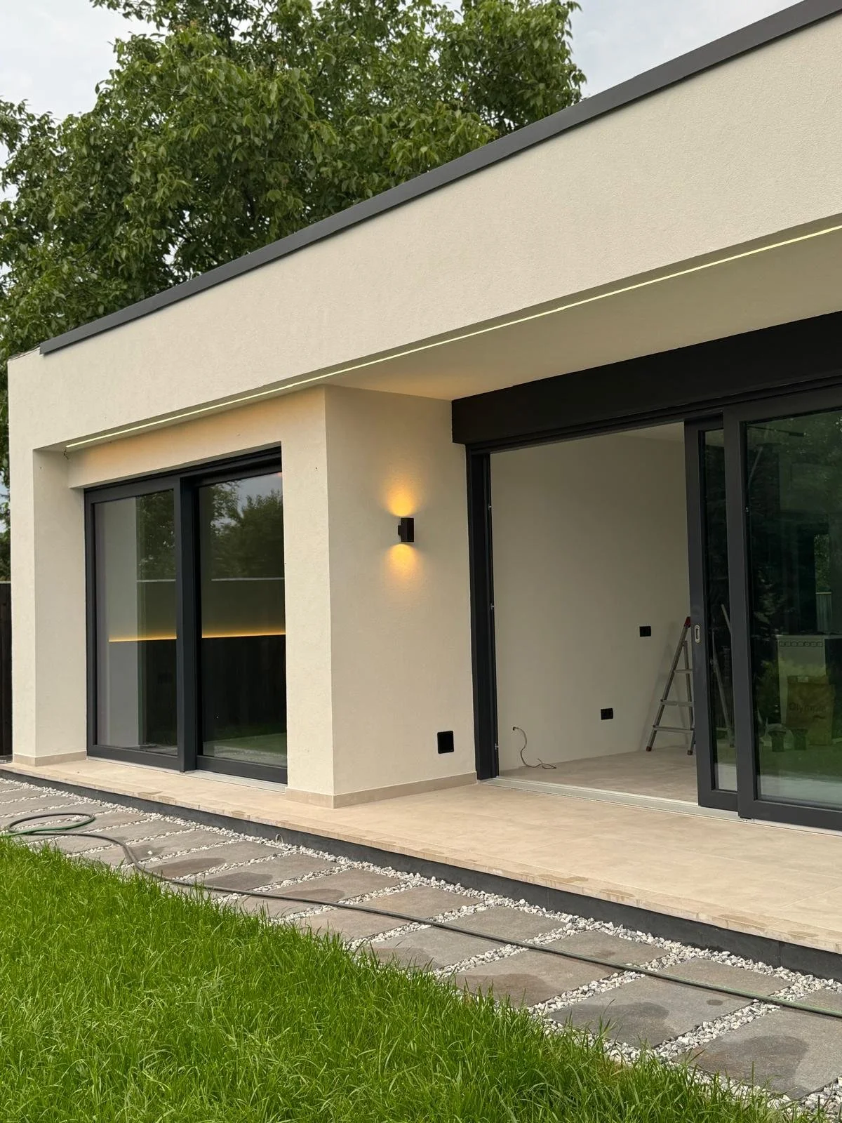 Modern house exterior with large sliding glass doors, a small porch, and a well-maintained lawn.