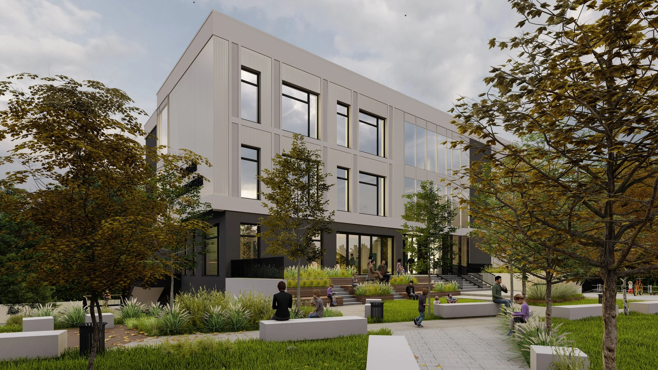 A modern multi-story building with large glass windows, surrounded by trees and a landscaped outdoor area with seating and people sitting and walking.