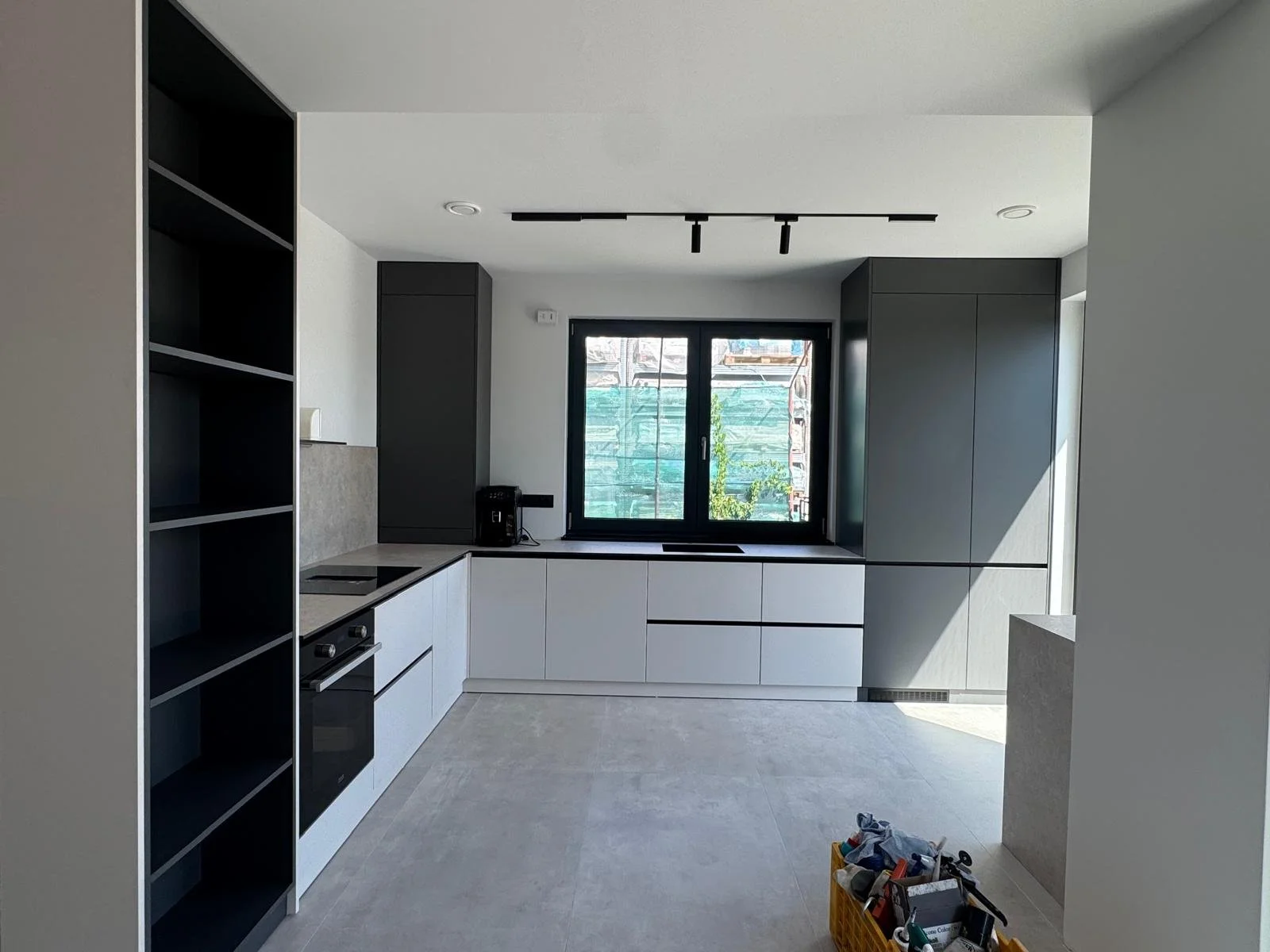 Modern kitchen with black and white cabinetry, a window above the countertop, and construction materials on the floor.