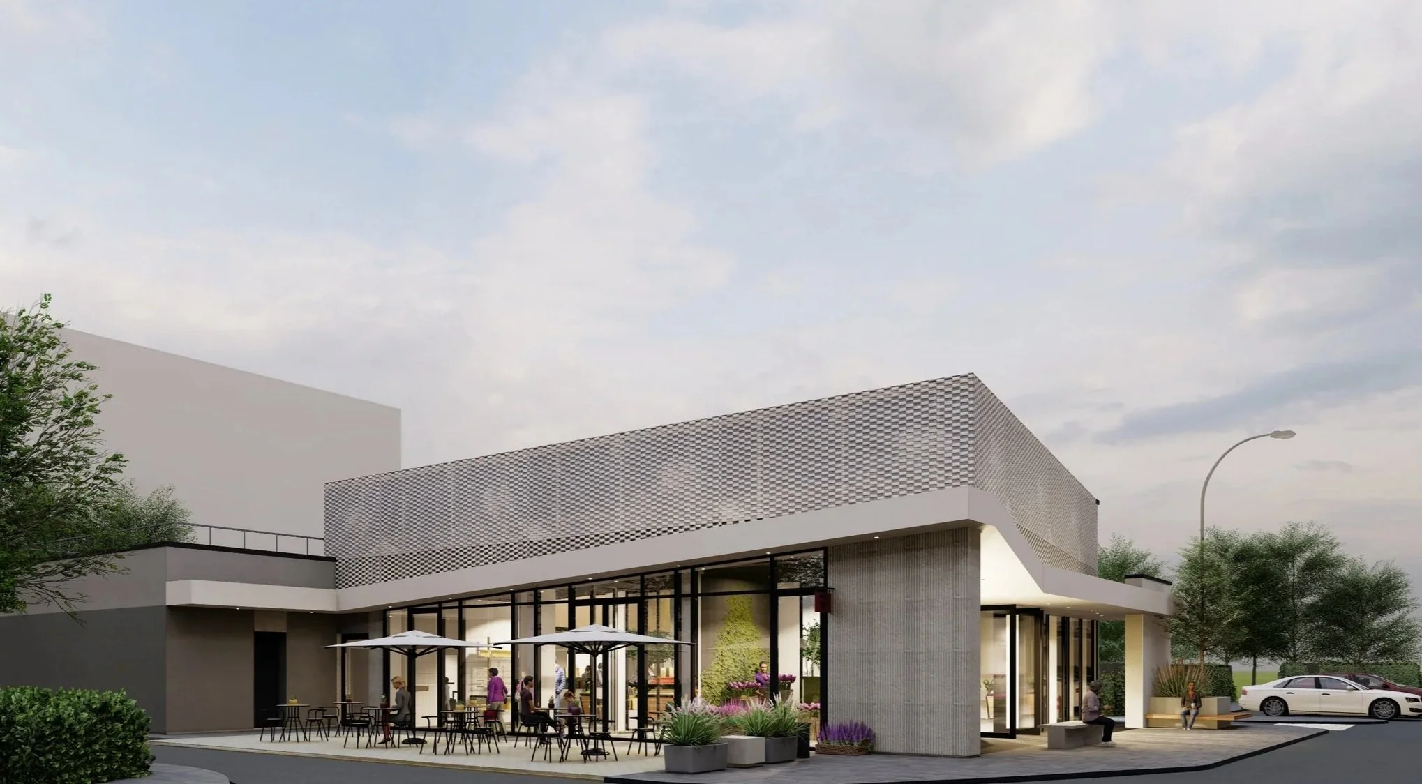 Modern cafe with outdoor seating, large glass windows, and a contemporary architectural design, with trees, a car, and people relaxing outside.