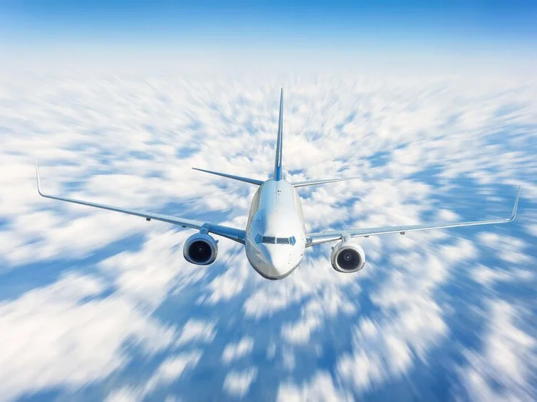 Un avion de ligne en vol haut dans le ciel, avec des nuages en dessous.