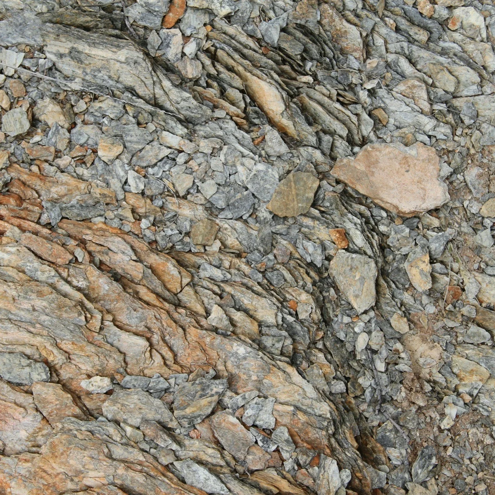 Close-up of a rock face with layered, jagged rocks and some smaller rocks scattered on the surface.