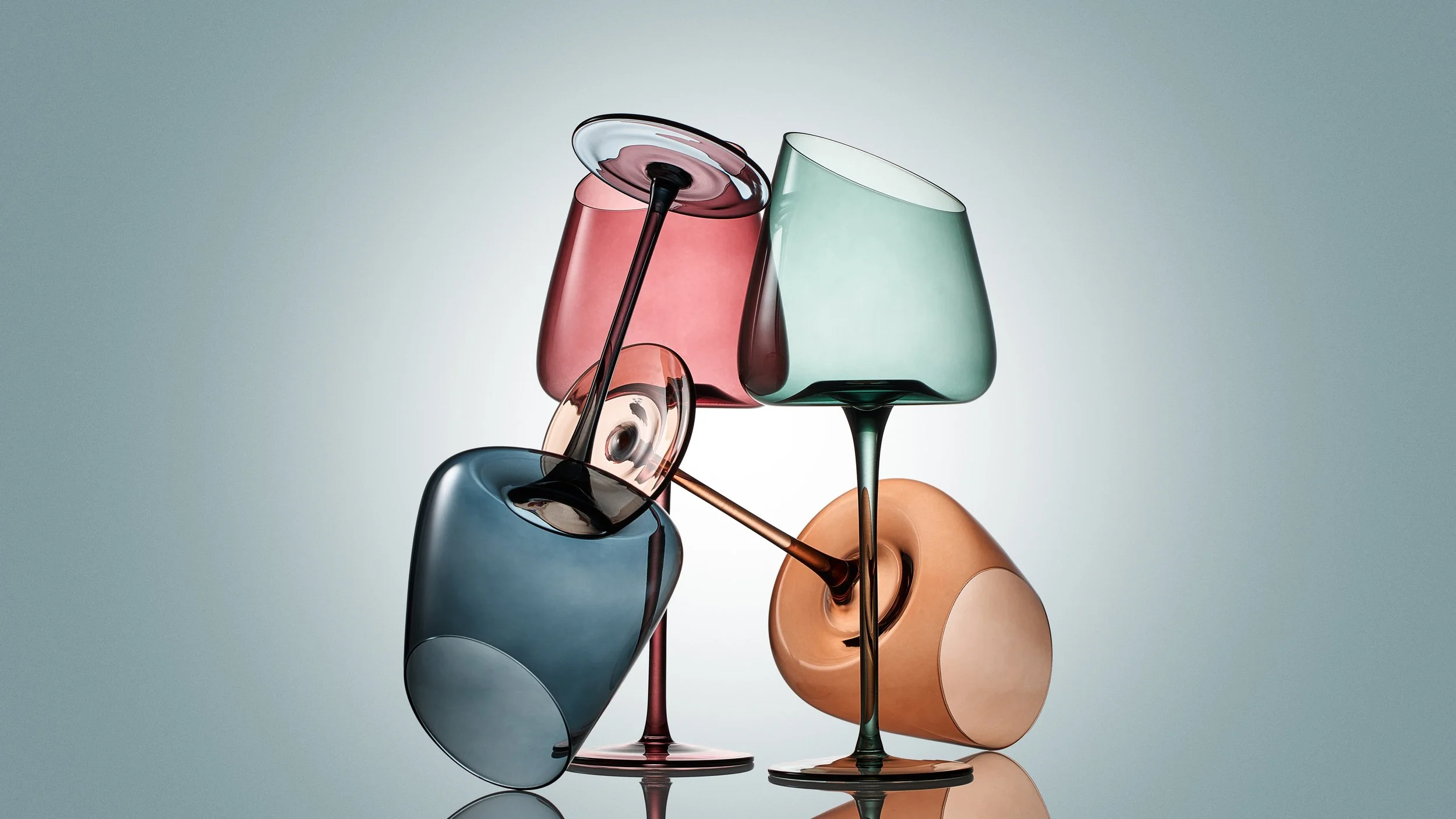 Colorful stacked glassware arrangement with pink, green, blue, and amber glasses in artistic display.