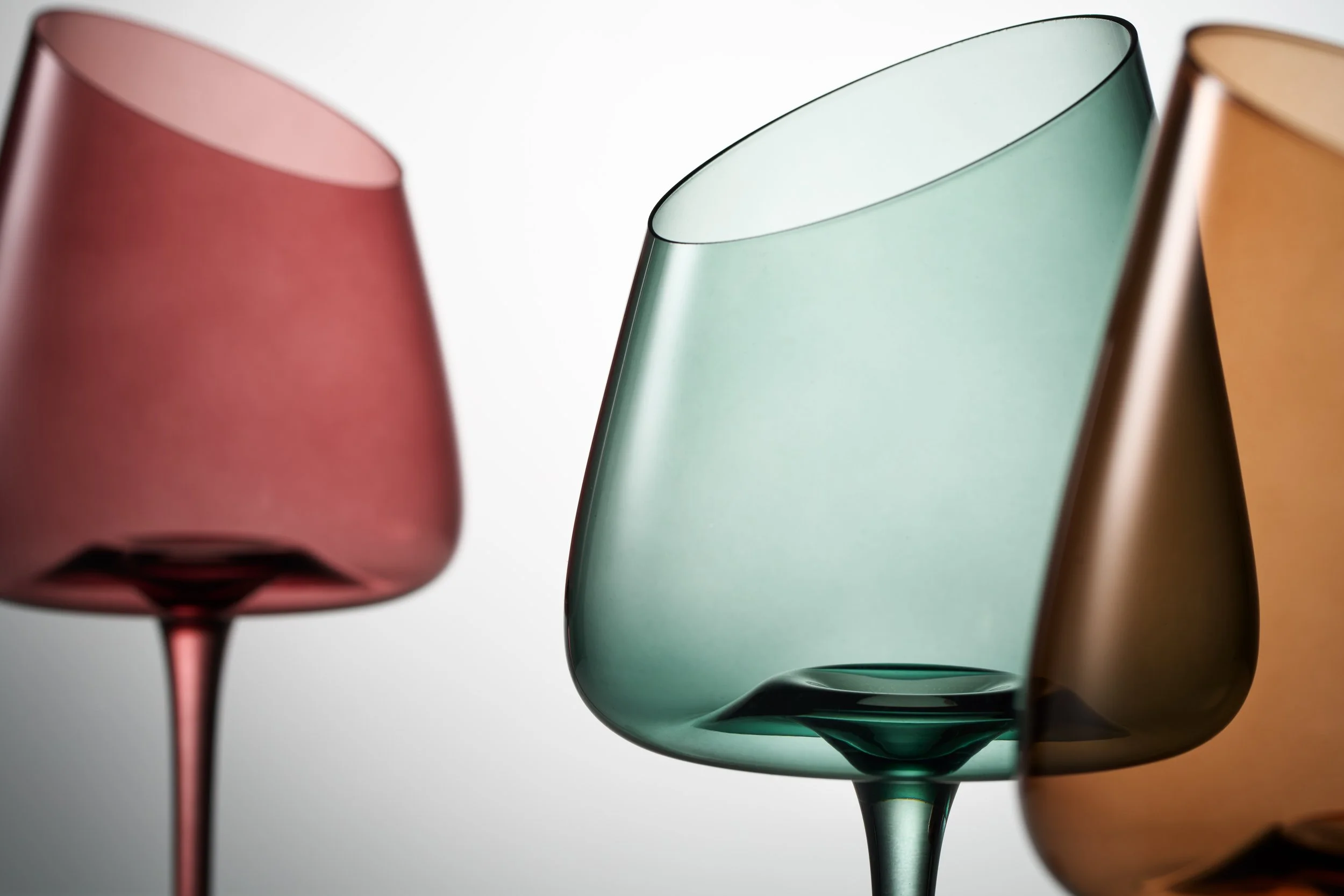 Close-up of three colorful glass wine glasses with different colored stems and bowls, positioned side by side.
