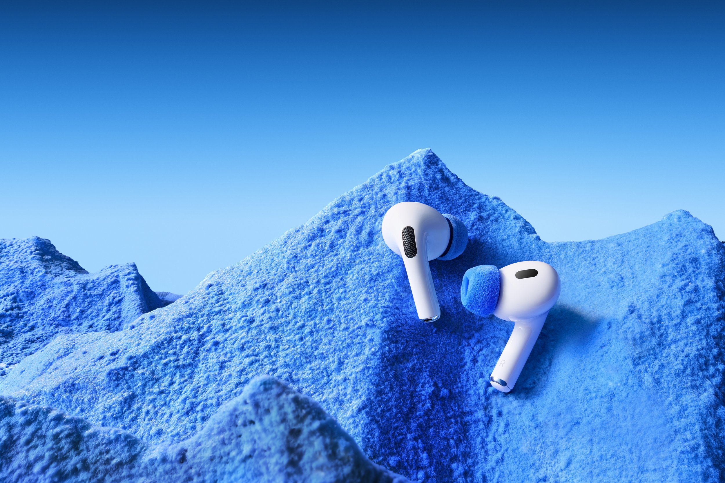 Wireless earbuds resting on a blue, snowy mountain peak with a clear blue sky in the background. creative photography. The best product photography studio in China