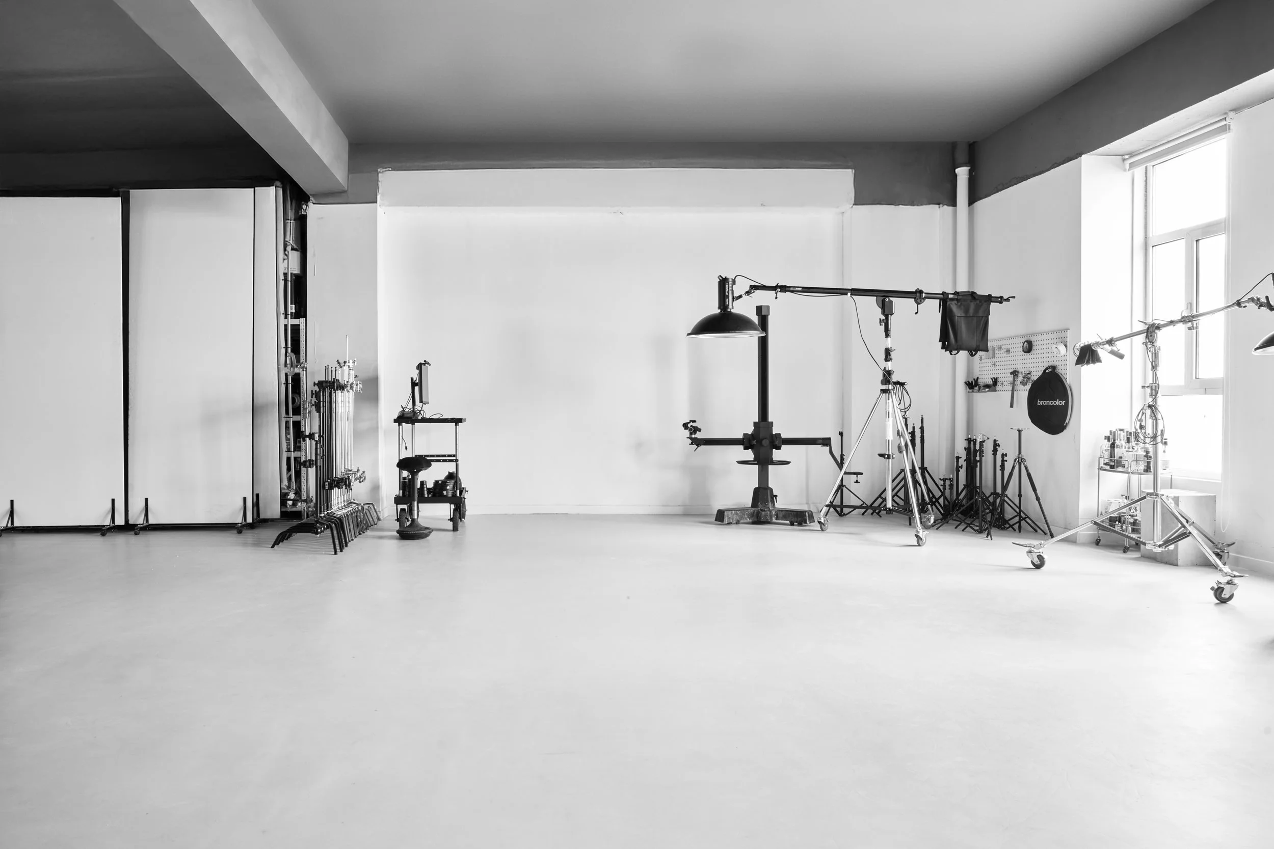 Photography studio with lighting and camera equipment, white backdrop, and large windows in grayscale.