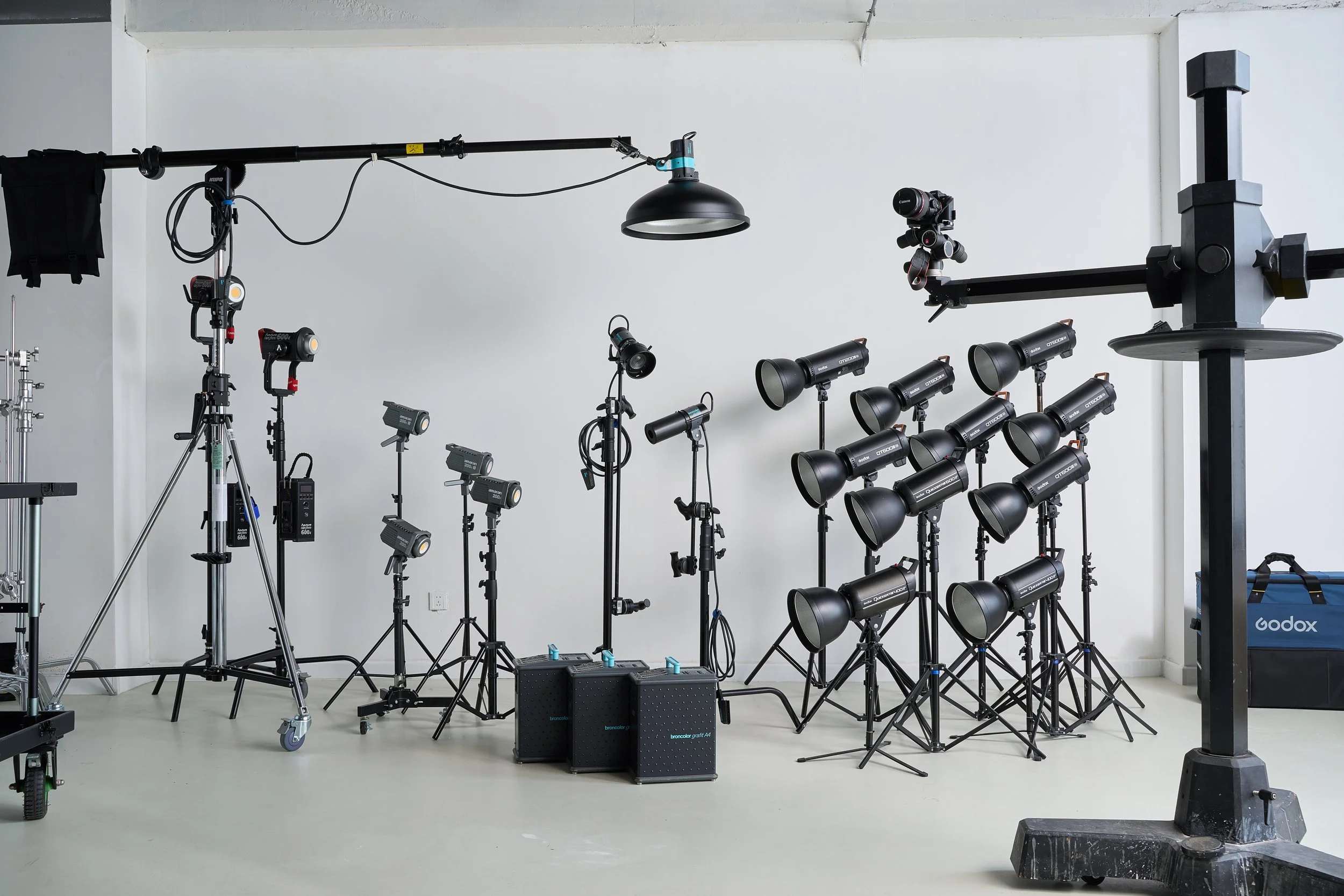 A photography studio setup with various lights, tripods, and equipment arranged in front of a plain white wall.