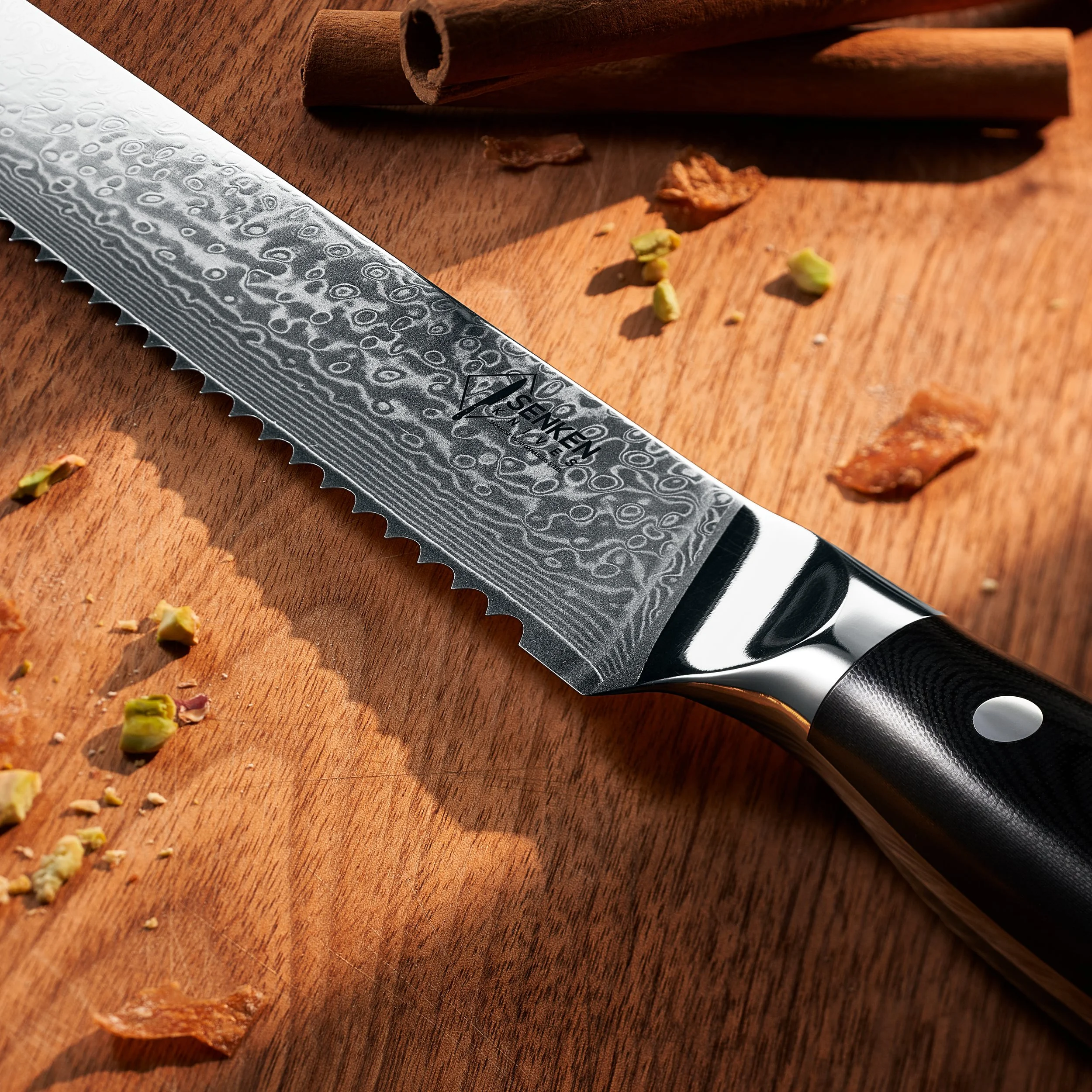 A close-up of a patterned kitchen knife resting on a wooden cutting board with crumbled pistachios and cinnamon sticks nearby. Chinese product photography studio