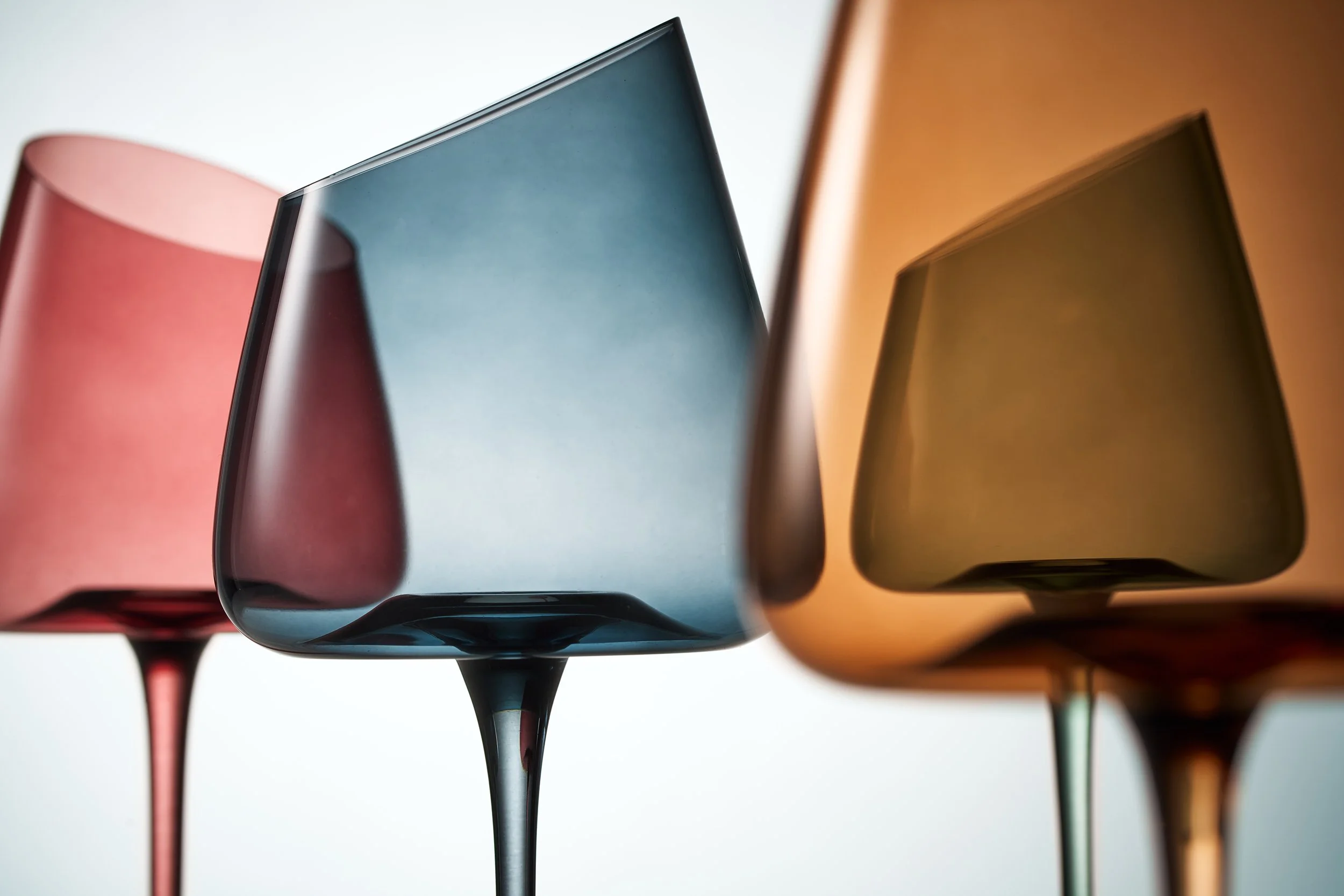 Close-up of three colorful, modern glass vases with curved shapes and metallic finishes, arranged in a row.