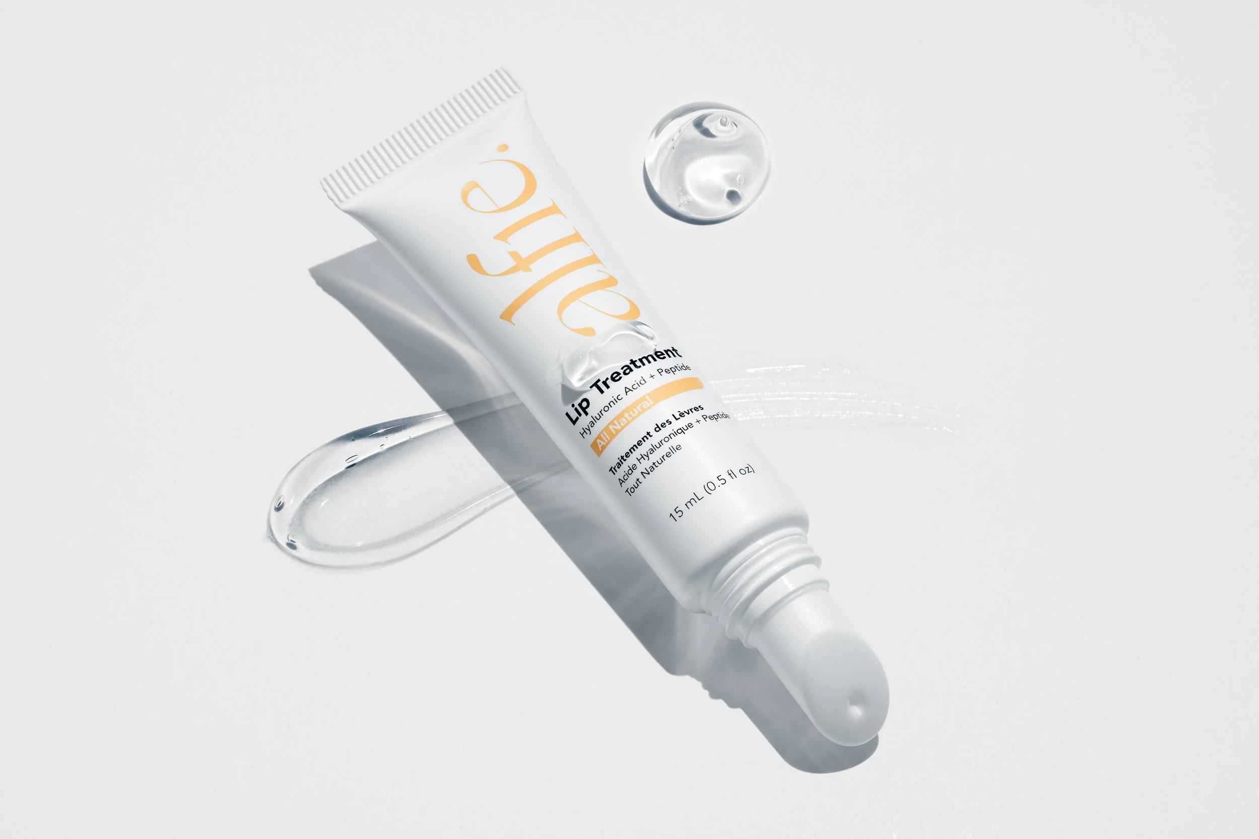 A tube of hyaluronic acid lip treatment with a dot of clear gel next to it on a white background.
