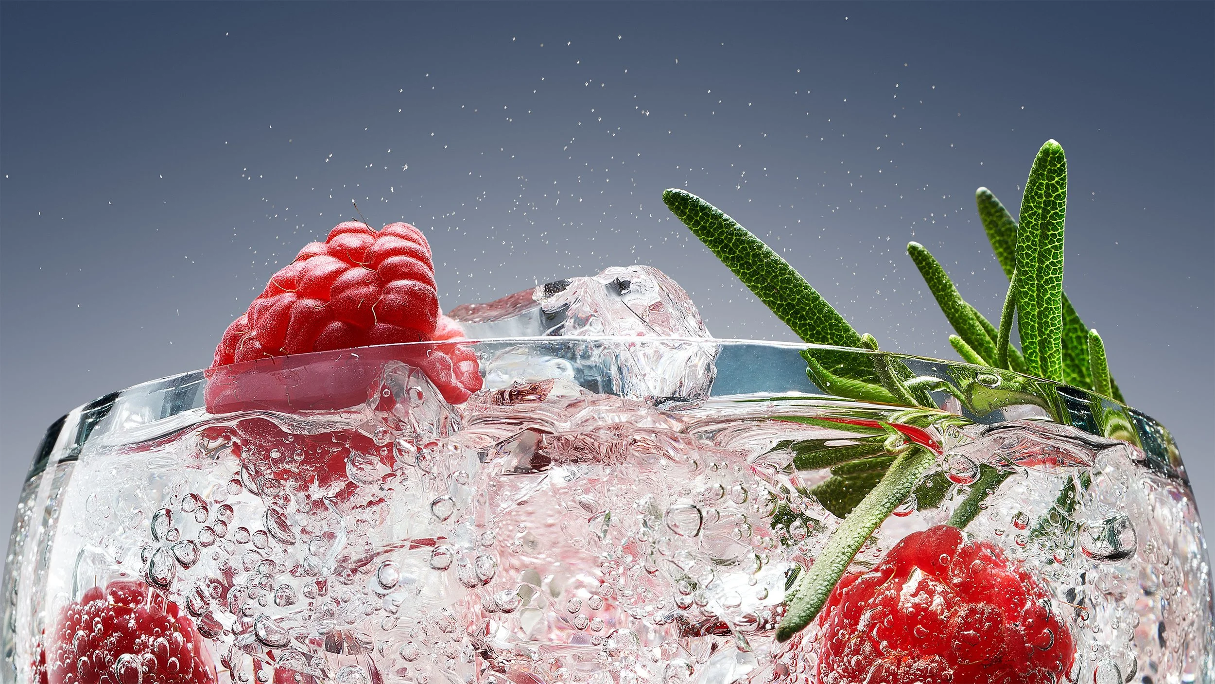 Raspberries and green herbs in a glass of sparkling water with bubbles and ice