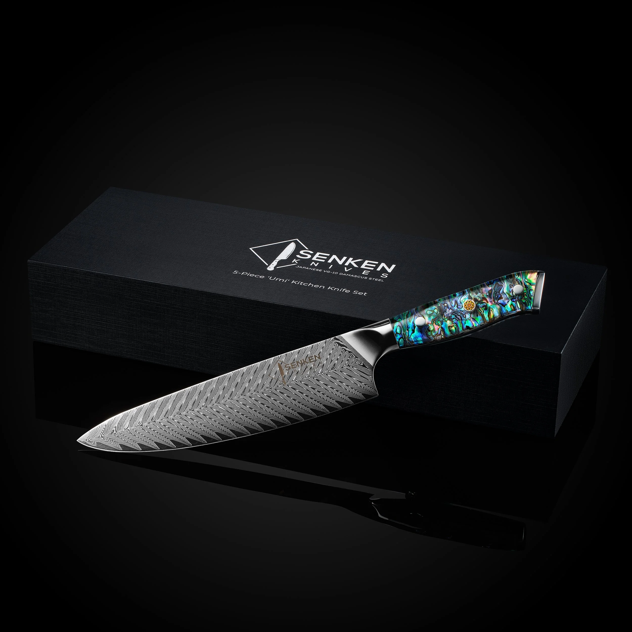 A decorative kitchen knife with a patterned green, blue, and black handle, placed on top of a black box with silver text branding it as a Senken knives set. The best product photography studio in China