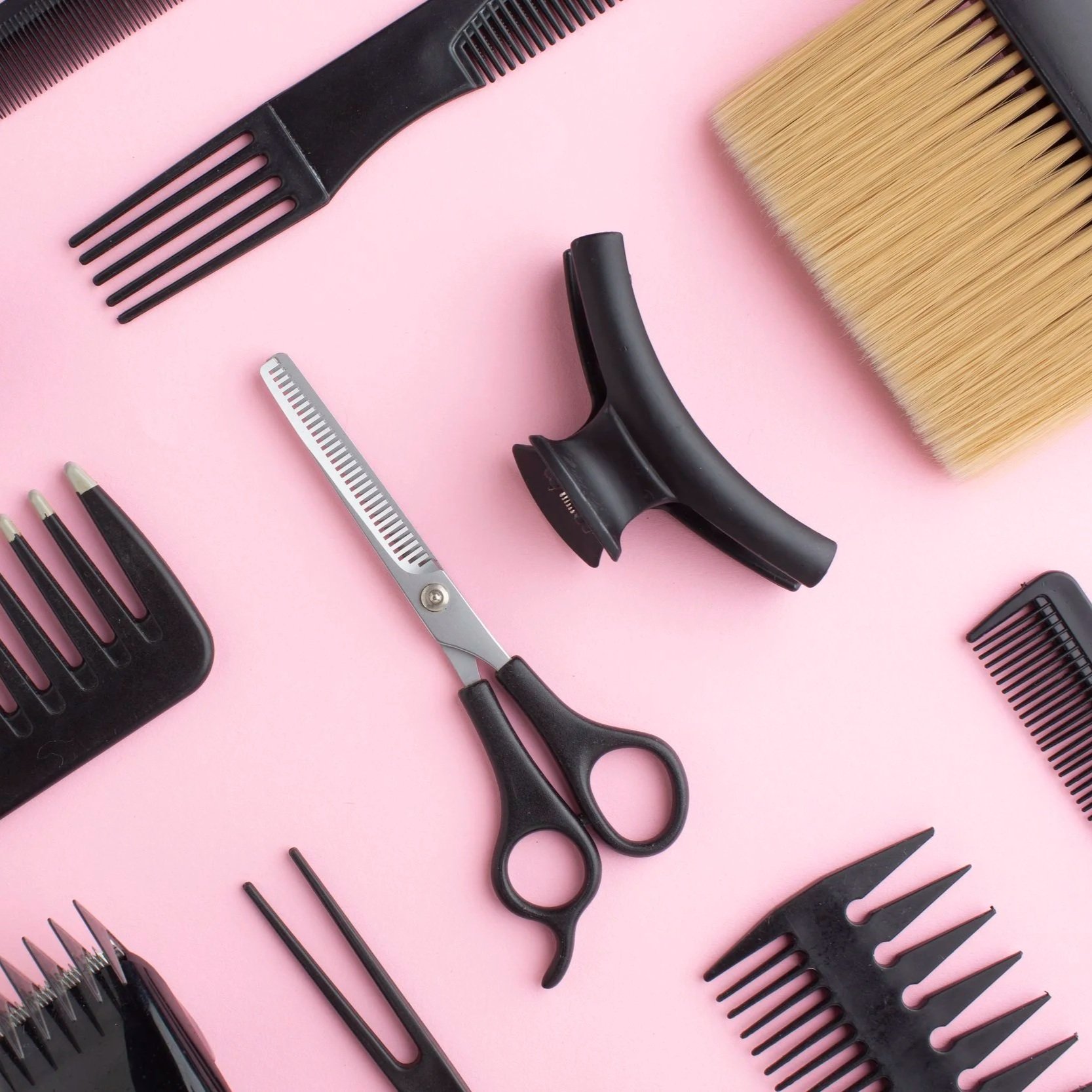 Saks, hårklype og hårbørster liggende flatt på rosa bakgrunn