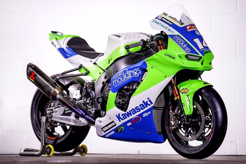Green, blue, and white Kawasaki racing motorcycle with sponsor decals, an aerodynamic windshield, and a carbon fiber exhaust, displayed on a stand against a white background.