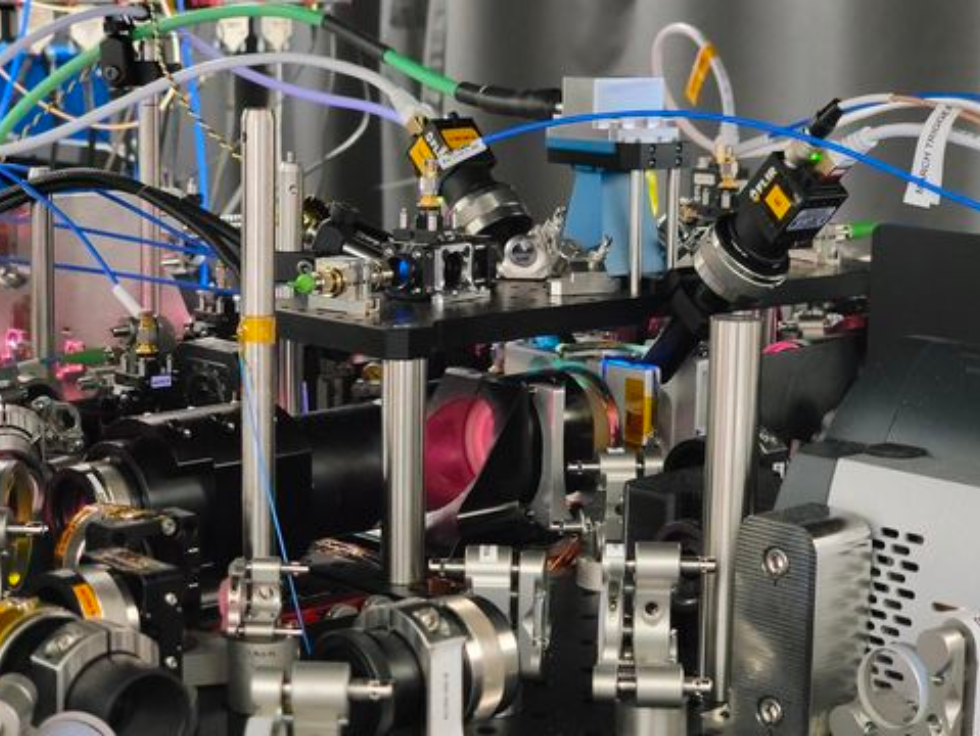 Close-up view of an advanced scientific laser system with various optical components, metal mounts, and colorful wires.