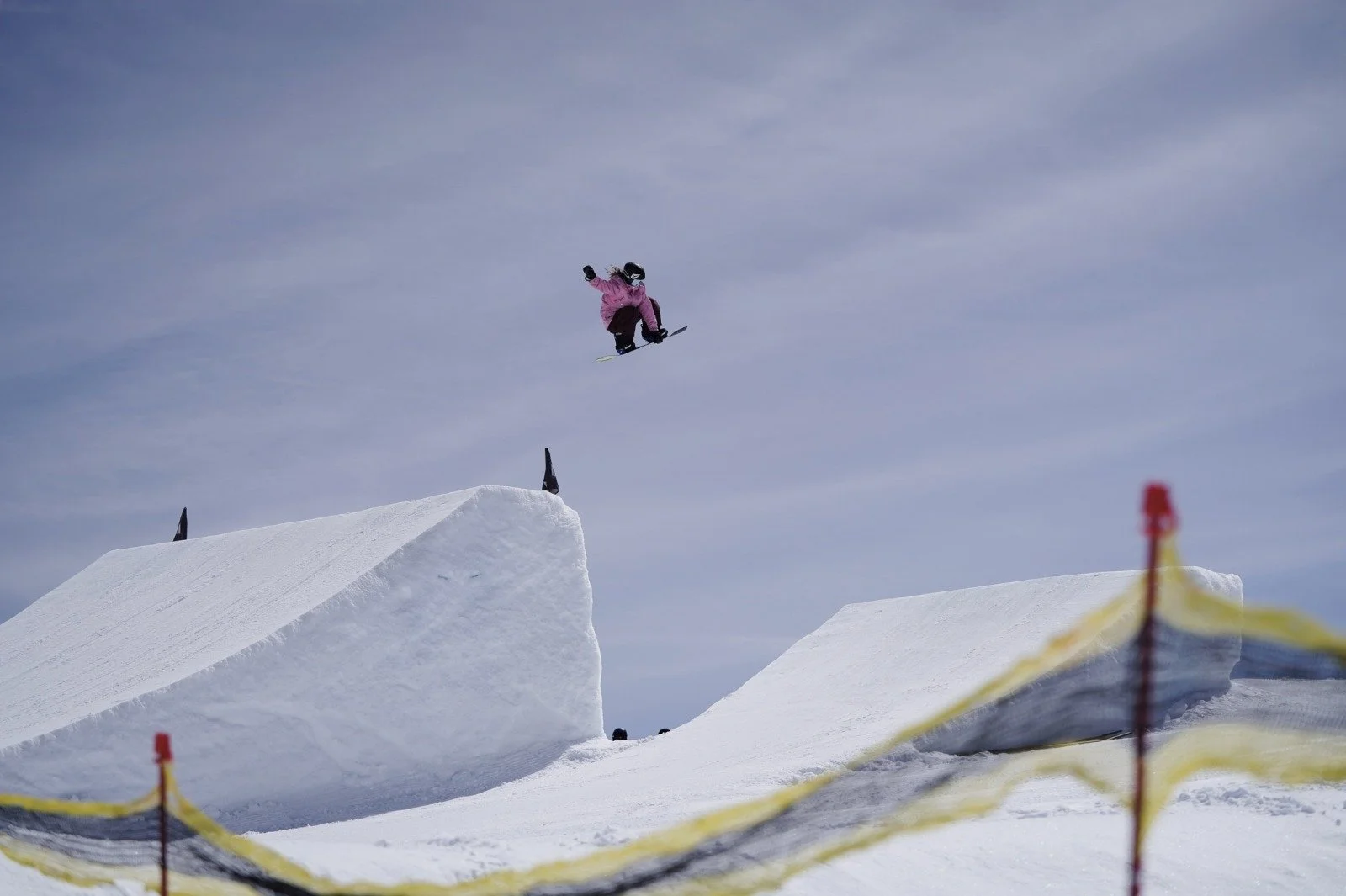 A female snowboarder flying over the end of a jump, doing a grab
