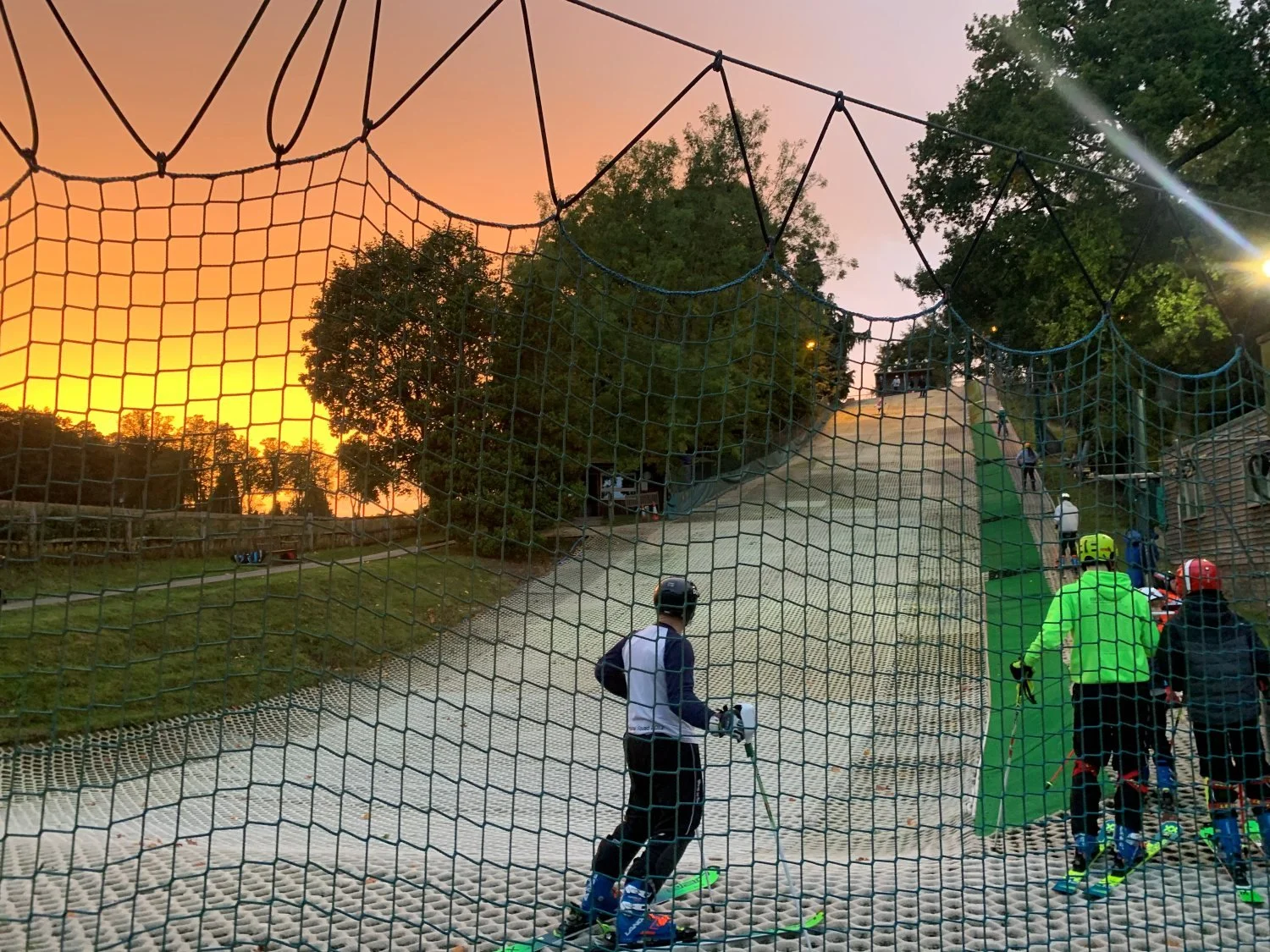 A male skiers stands at bottom of dry slope looking at sunset