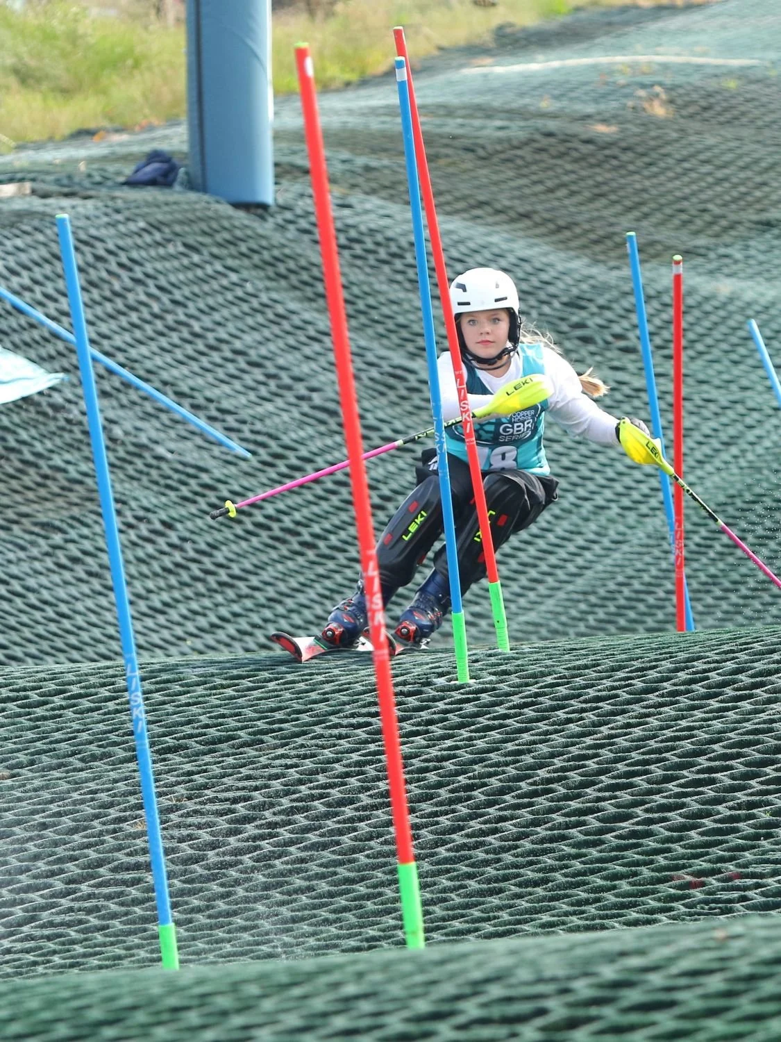 A young female ski racer racing down a dry slope slalom course