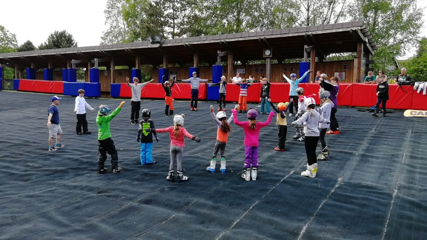 A group of children being taught a warm up exercise by a ski instructor at a dry slope