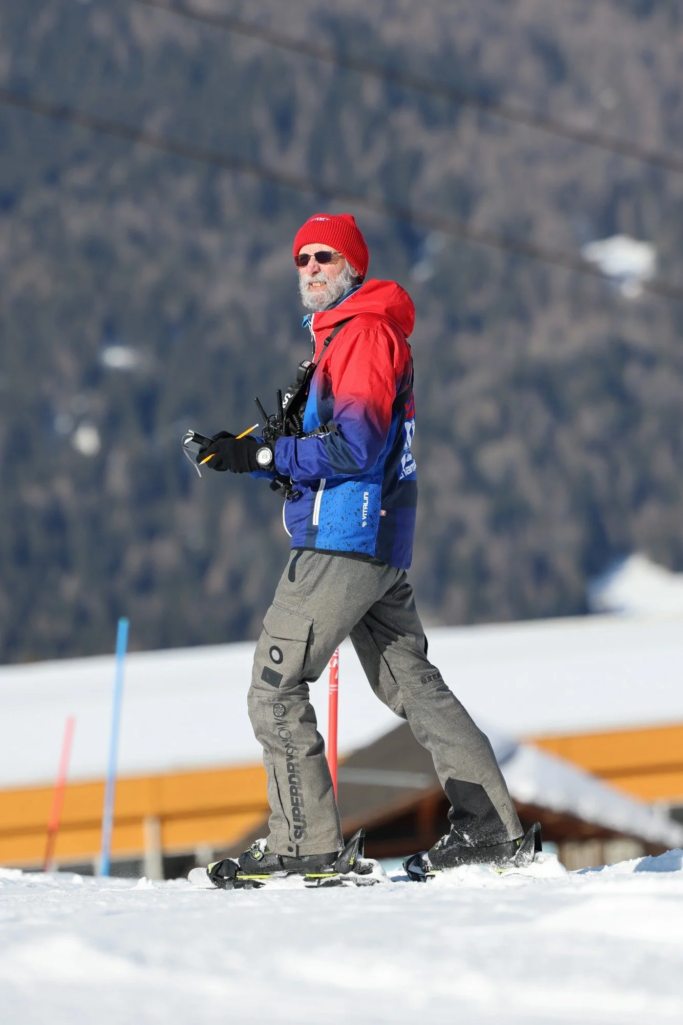 A male skier with a clipboard standing on a snowy race slope