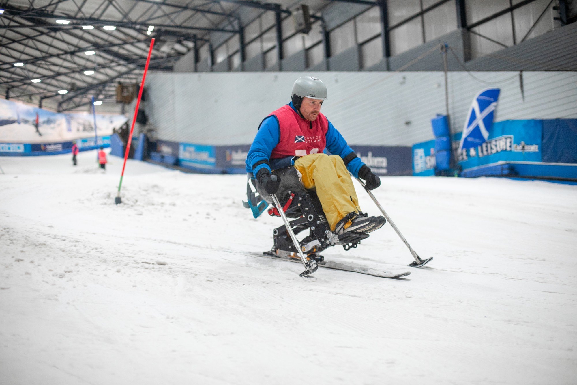 A man in a sit ski skiing down an indoor snow centre slope
