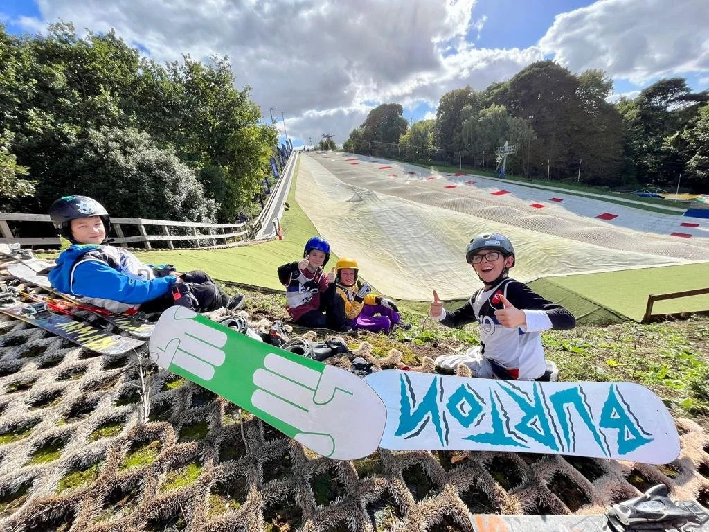 Four young snowboarders sitting on the ground at a dry slope