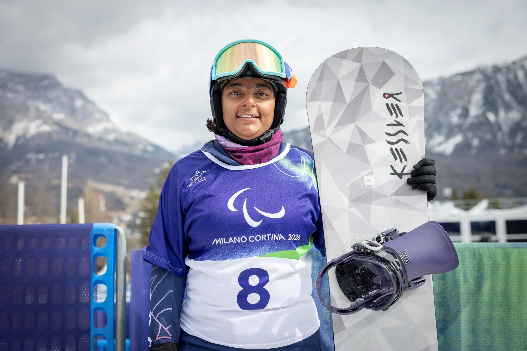 A female paralympic snowboarder stands in snow holding her snowboard