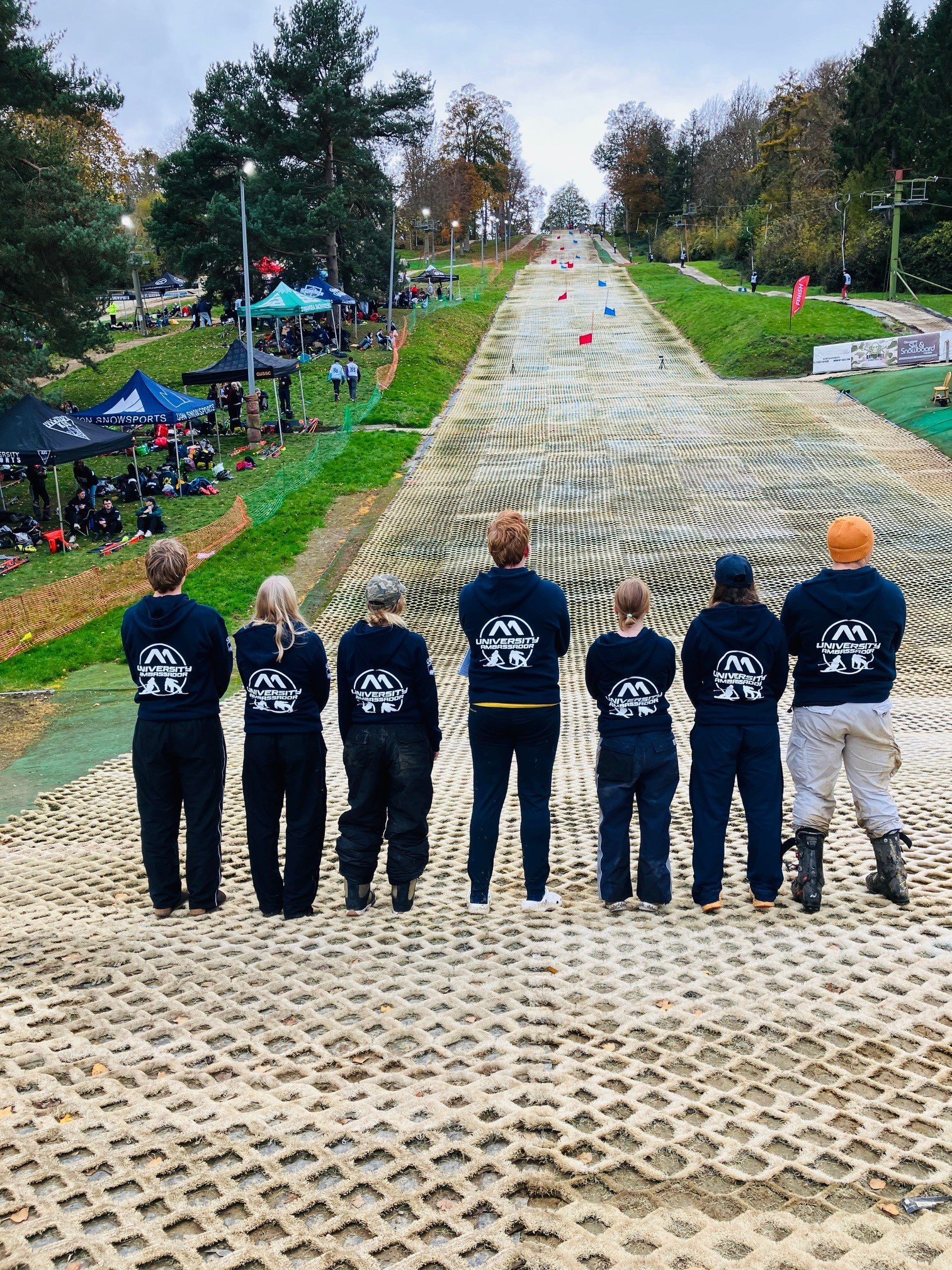 A group of seven university students with backs to the slope, watching a dry slope alpine race