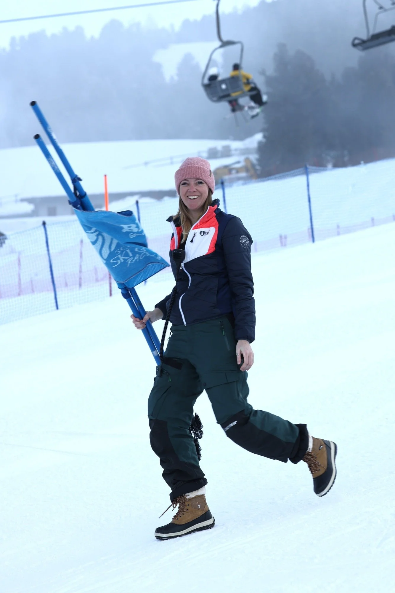 A female official carrying alpine race gates on a snowy race course