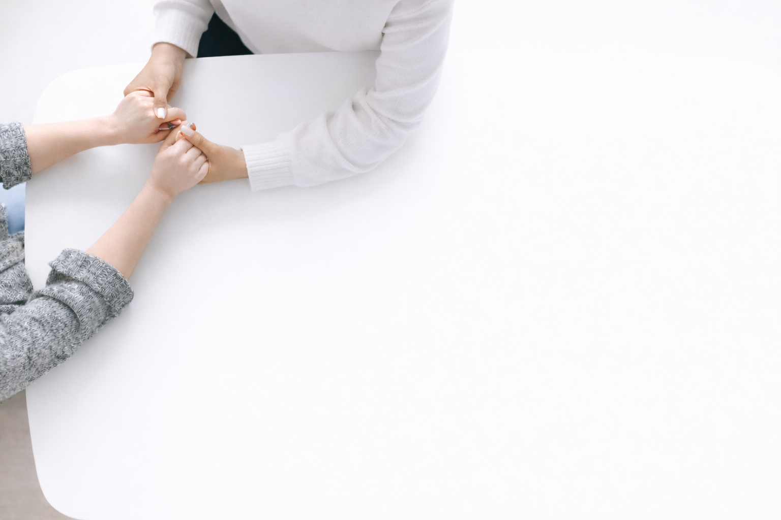 Two people holding hands across a white table.