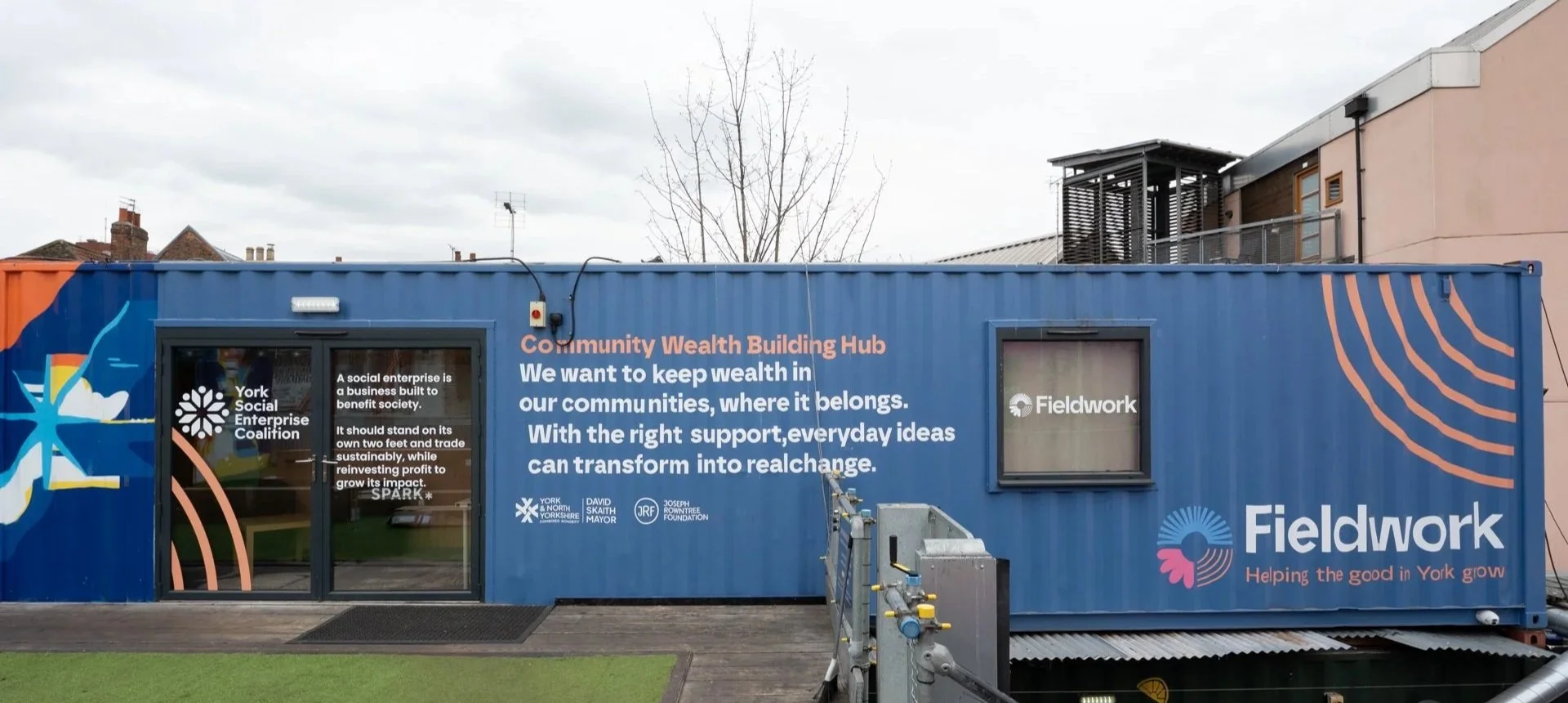 A shipping container unit with the words Community Wealth Building Hub written on it