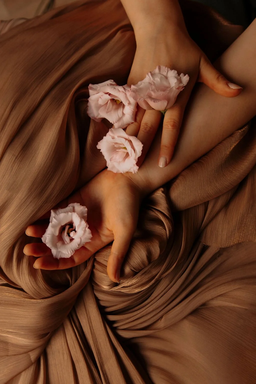 Deux mains entrelacées posées sur un tissu de couleur beige, décorées avec des fleurs roses enroulées autour des doigts.