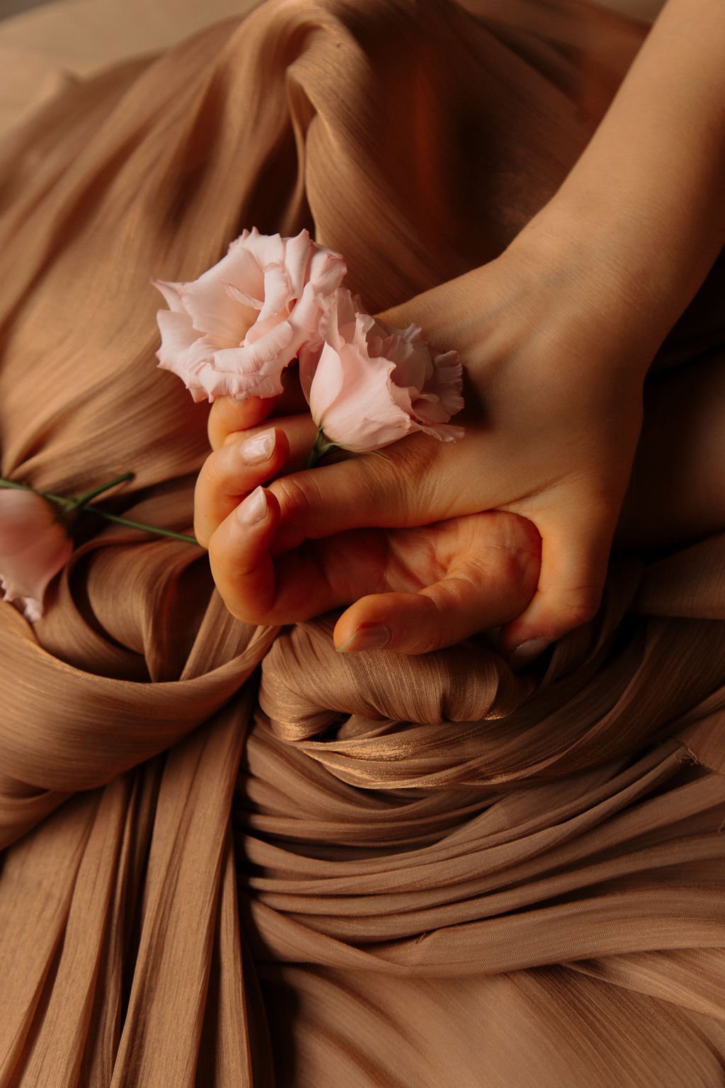Une main tenant un bouquet de fleurs roses, posée sur un tissu ou un vêtement de couleur nude ou beige avec des plis.