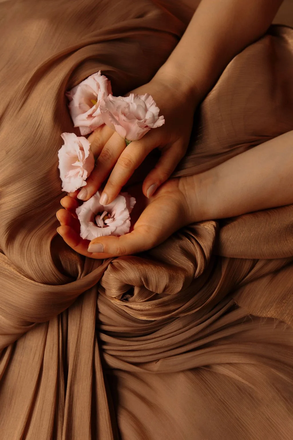 Mains tenant des fleurs roses, posé sur un tissu en satin marron avec des plis et des drapés.