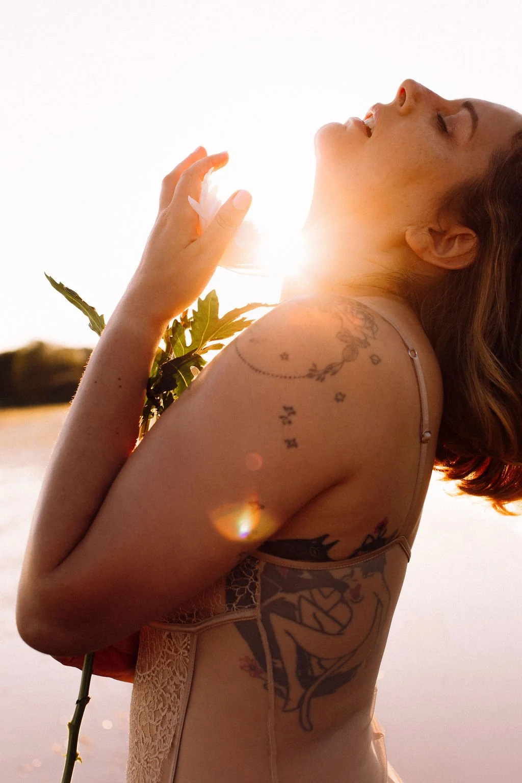 Portrait d'Alice Alma, tenant une rose, se tenant dans une lumière de coucher de soleil avec un lac en arrière-plan.