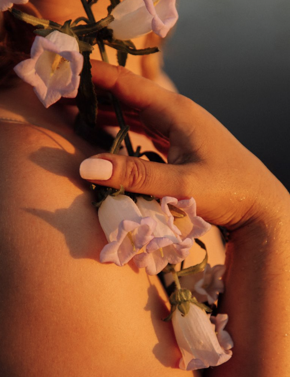 Main qui tient une couronne de fleurs blanches et roses, éclairée par une lumière chaude, avec un fond flou.