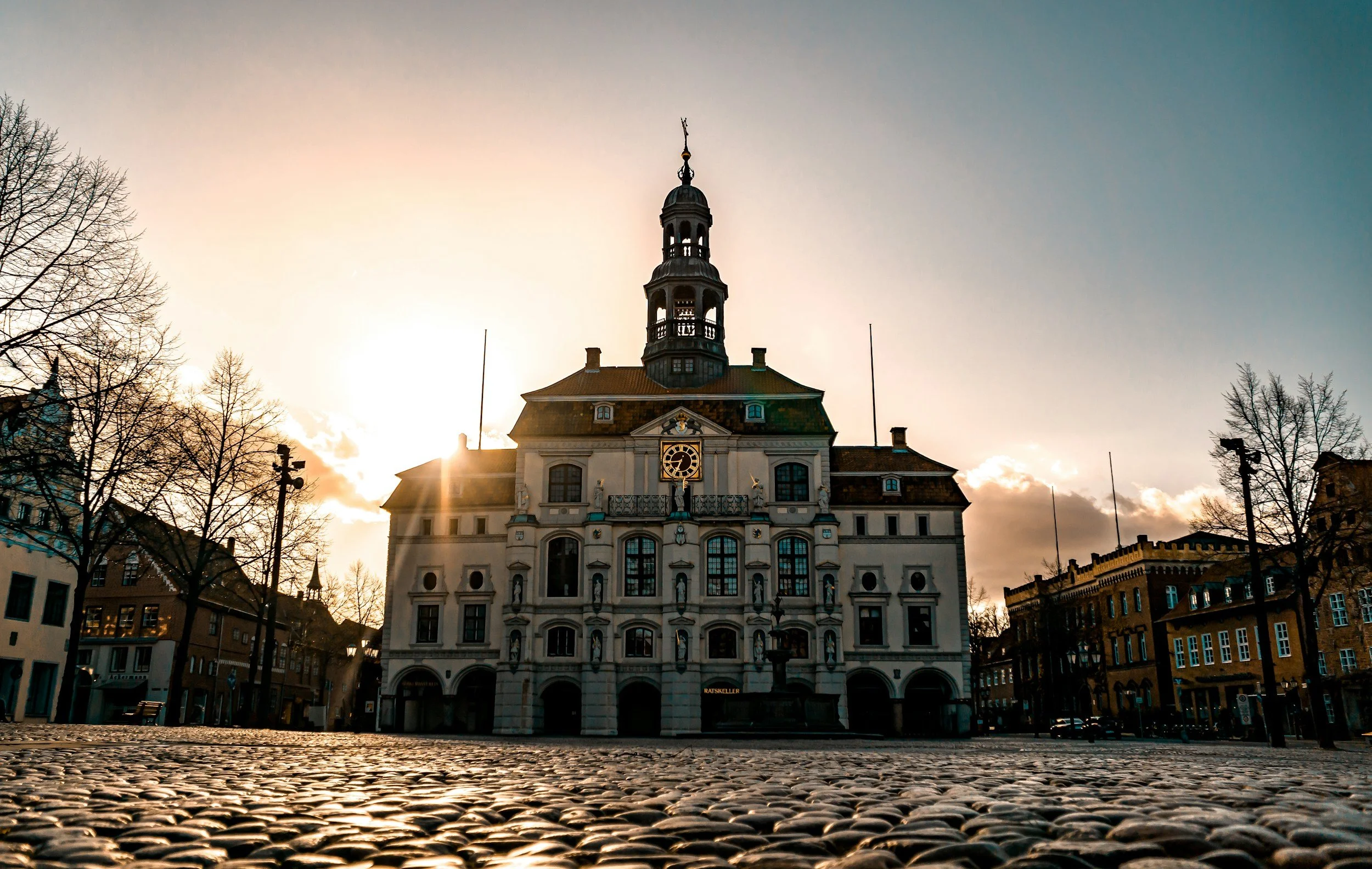 Historisches Gebäude in der Abendsonne mit cobbelsteinertem Platz im Vordergrund.