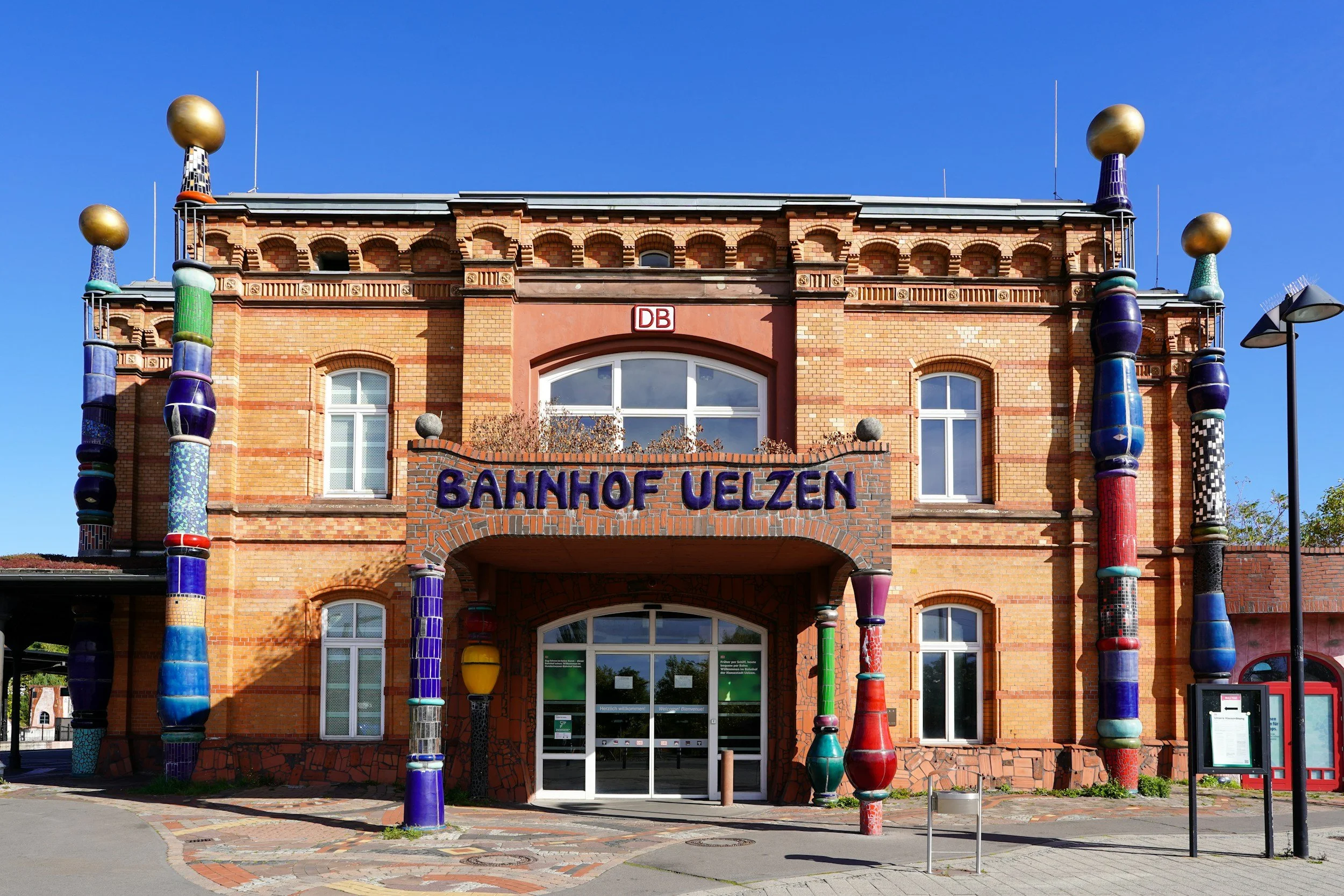 Das Gebäude des Bahnhofs Uelzen ist ein mehrstöckiges Backsteingebäude mit bunten, skurril gestalteten Säulen und einer auffälligen Beschilderung.