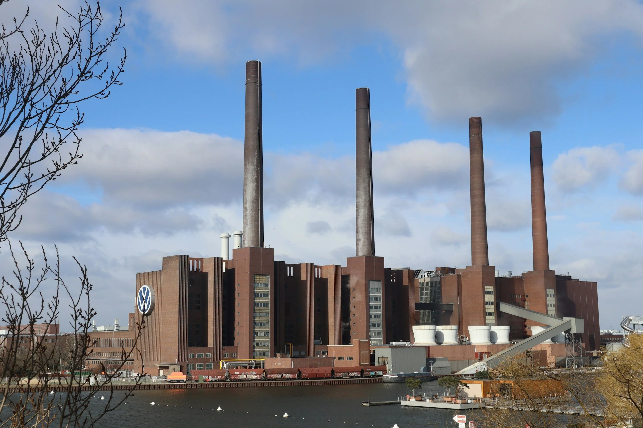 Das Bild zeigt das VW Werk in Wolfsburg mit vier Schornsteinen gegen einen Himmel mit Wolken.