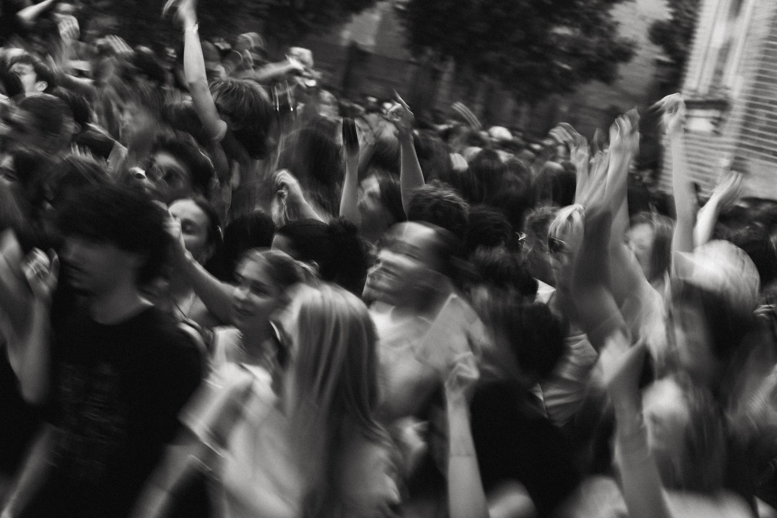 Une foule dense de personnes dans une rue, certaines levant la main, la plupart se semblant être en mouvement, dans une scène probablement de rassemblement ou de manifestation.