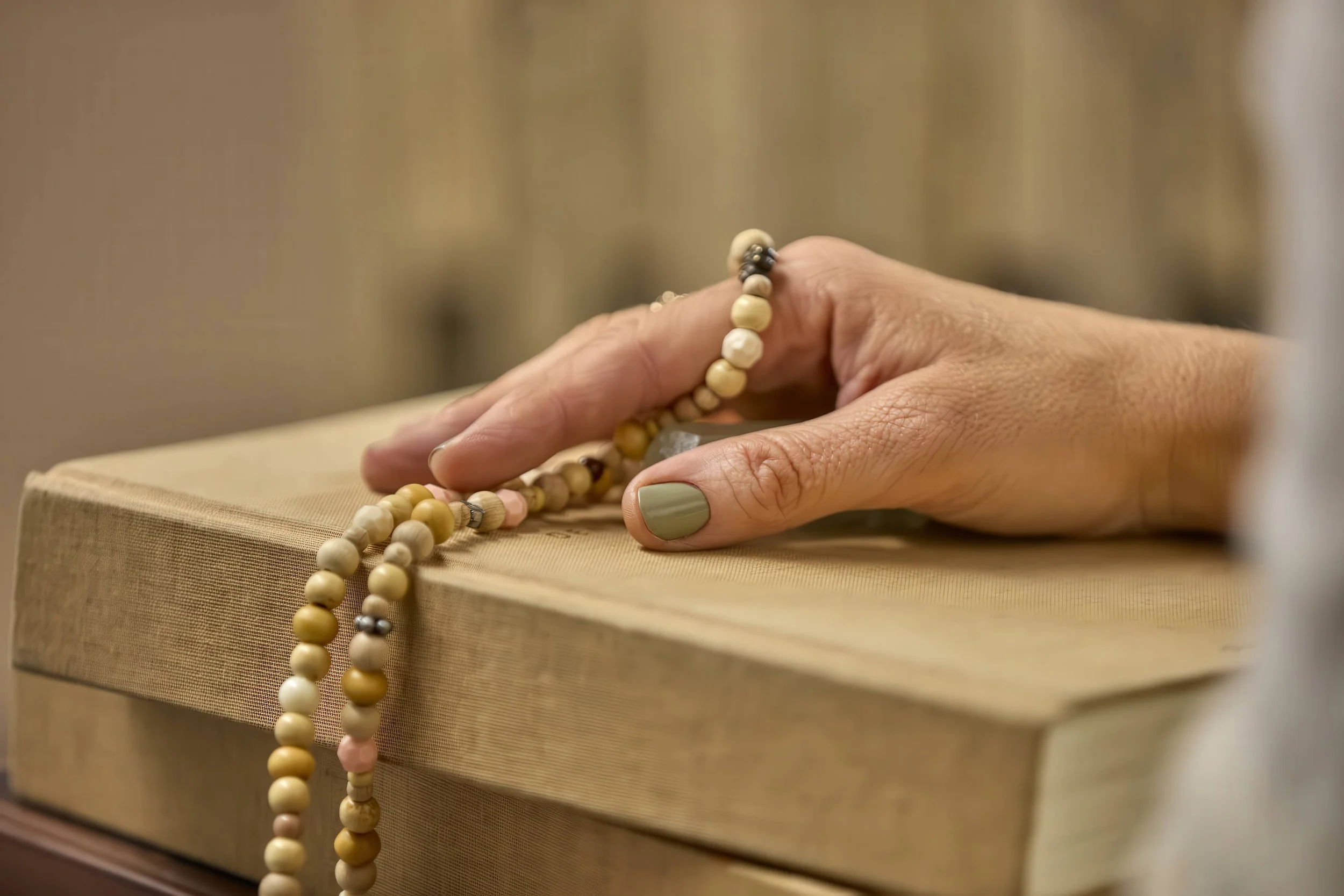 Hånd, der rører ved en bønnekrans på en bog.