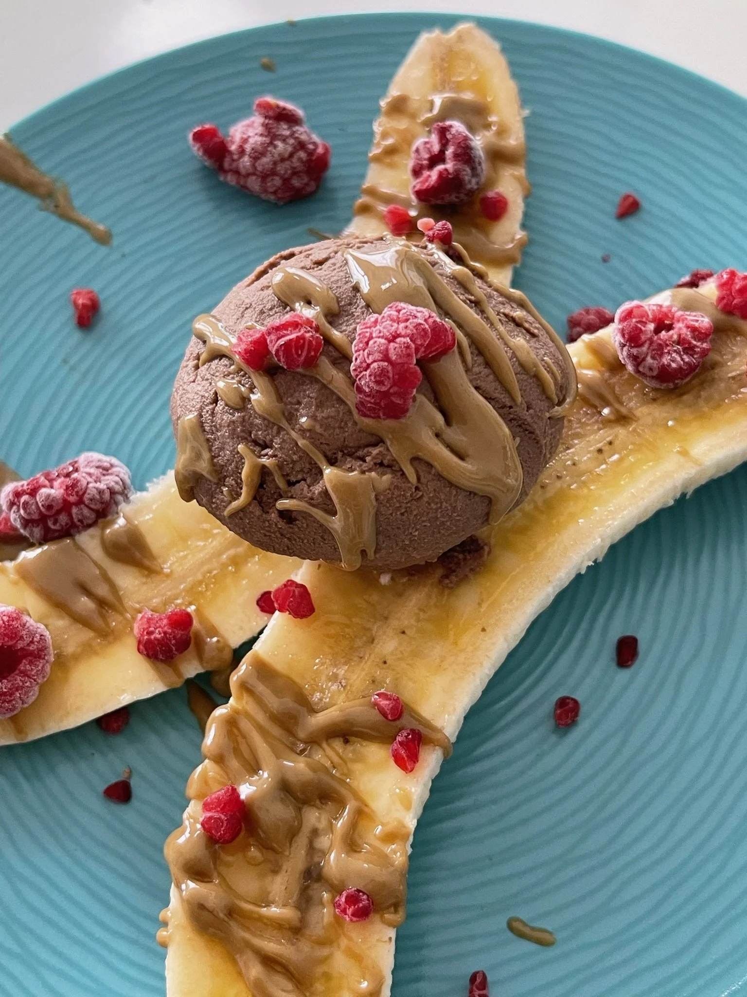 Sliced banana topped with chocolate ice cream, red berries, caramel drizzle, on a blue plate.