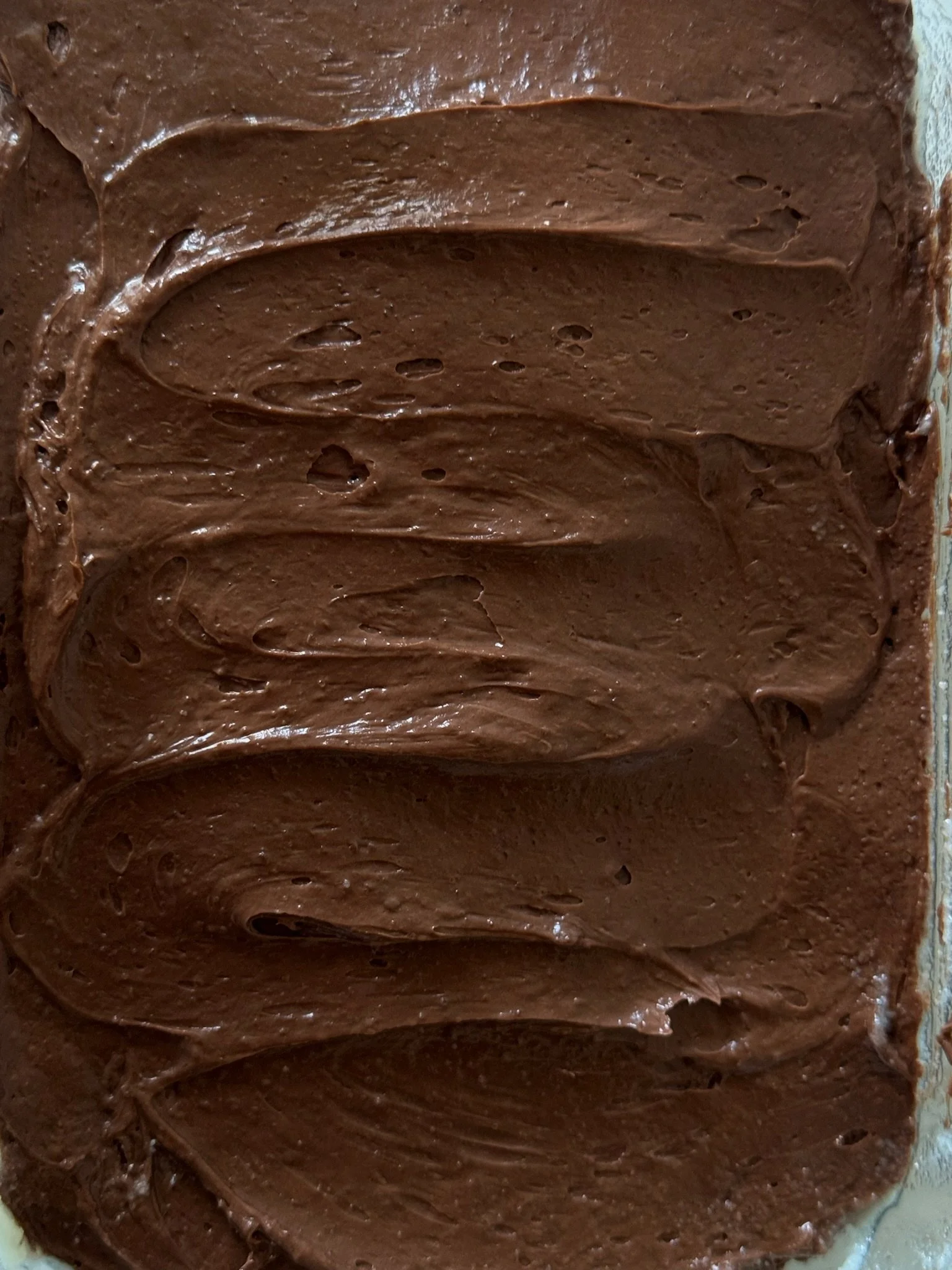 Close-up of chocolate frosting spread evenly on a surface, with a smooth and shiny texture.