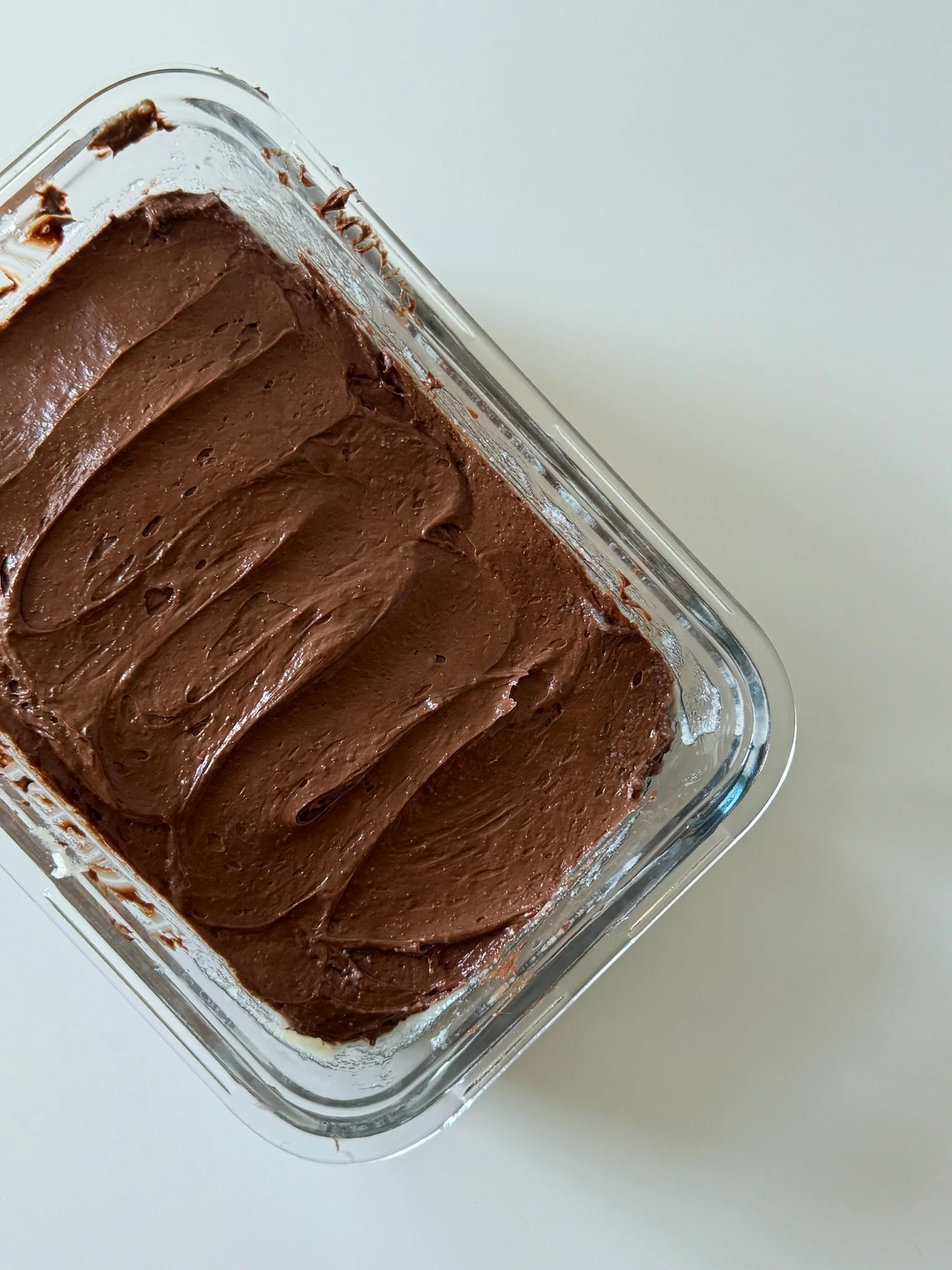 A glass container with finished chocolate mousse on a white surface.