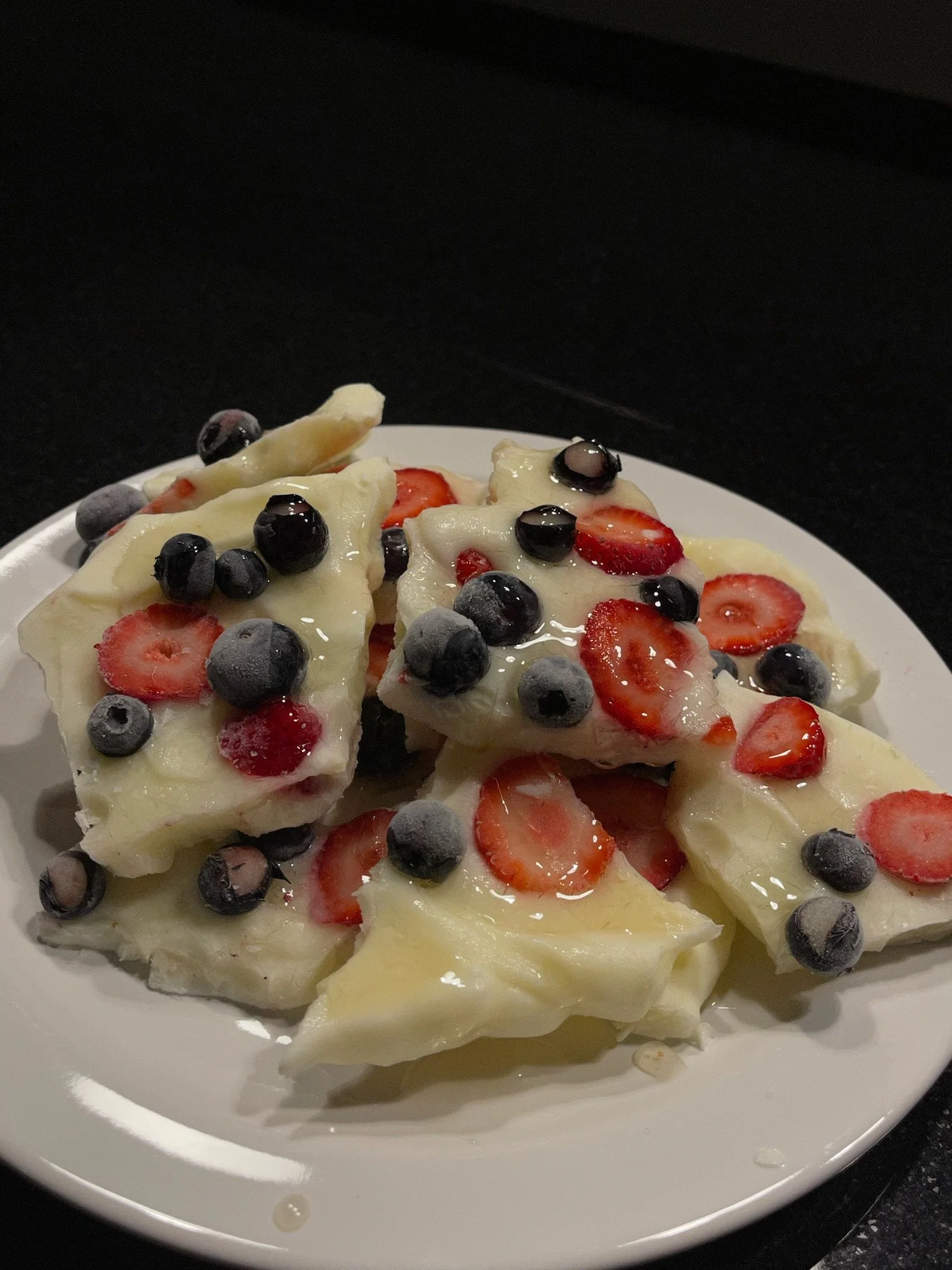A white plate of cheese topped with strawberries and blueberries, drizzled with honey.