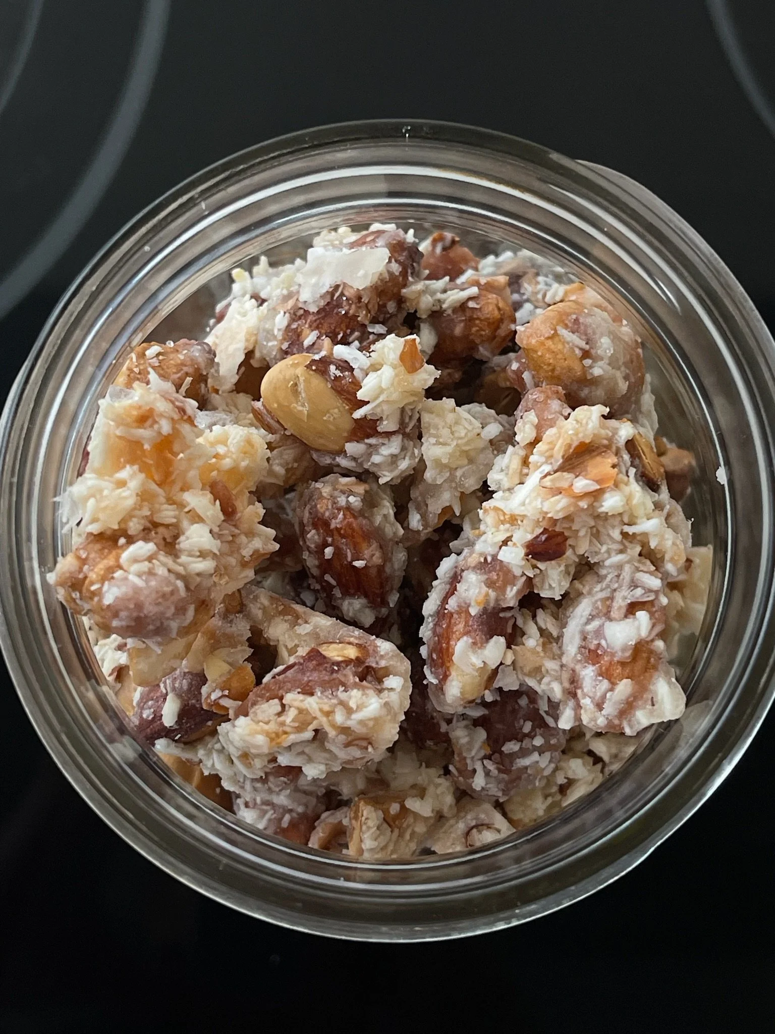 A glass jar filled with a mix of caramel popcorn, coated nuts, and white chocolate pieces.